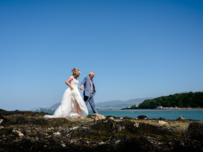Bride and groom walking on the Menai Strait shore