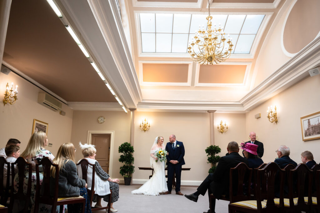 Bride and groom walking down the ailse in the Sir A Brumwell Thomas room at Stockport Town Hall