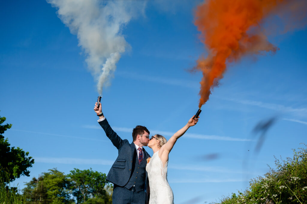 Bride and groom kissing while holding a white and orange smoke grenade