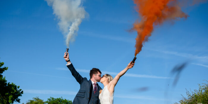 Bride and groom kissing while holding a white and orange smoke grenade