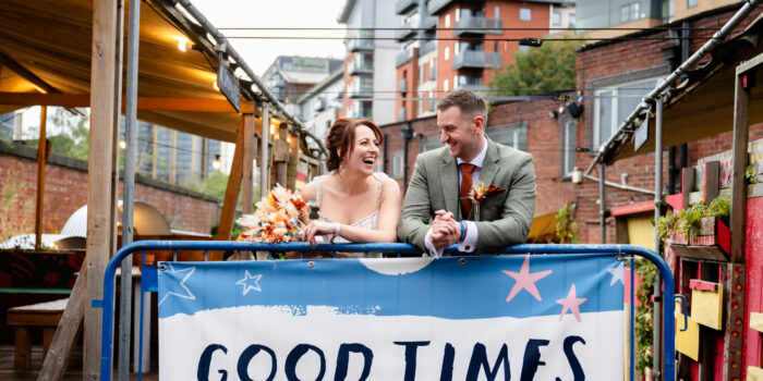 Bride and groom posiging in front of a sign that says Good times