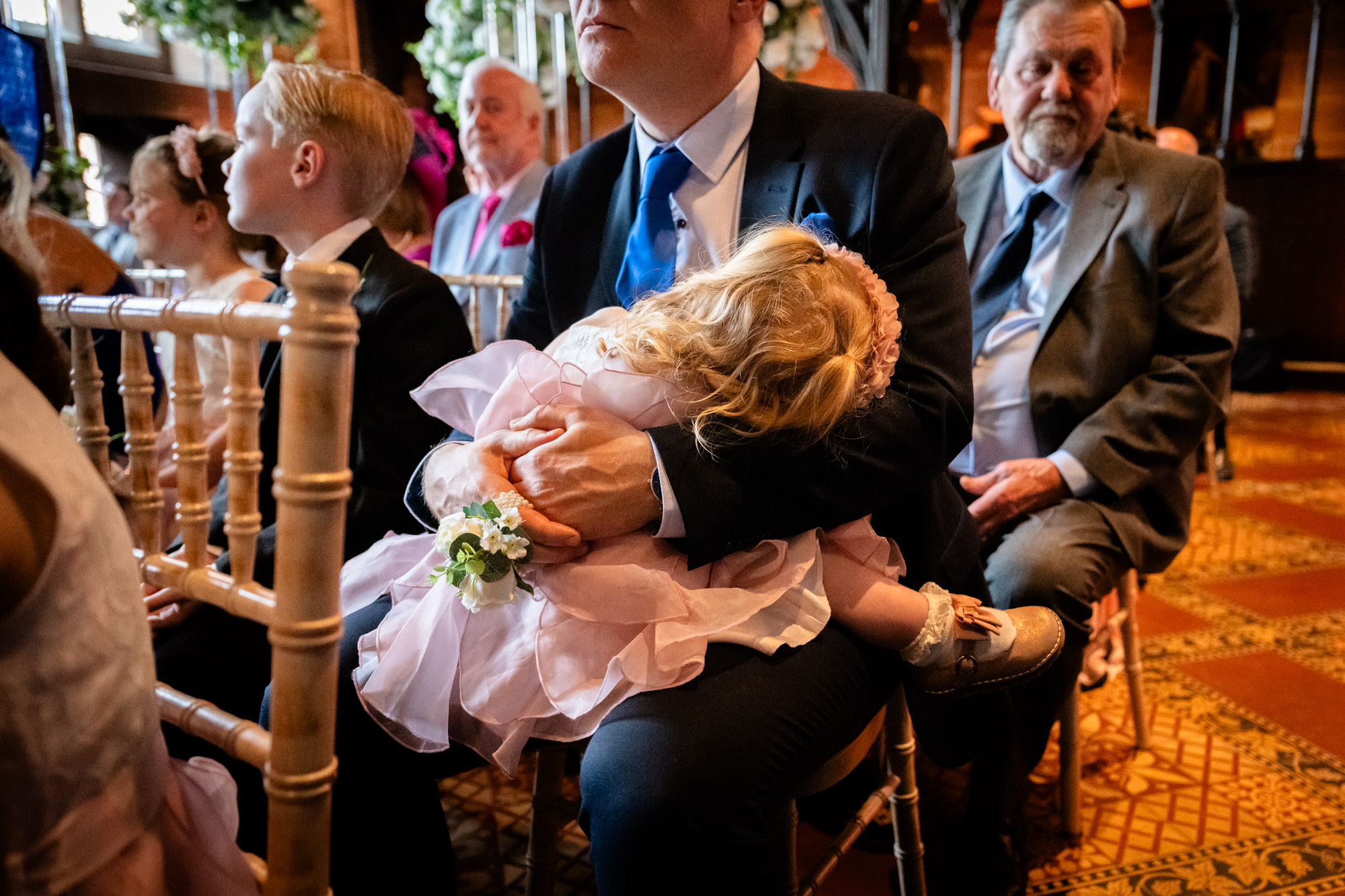 Little girl sleeping on her dad's lap during the ceremony at Peckforton Castle