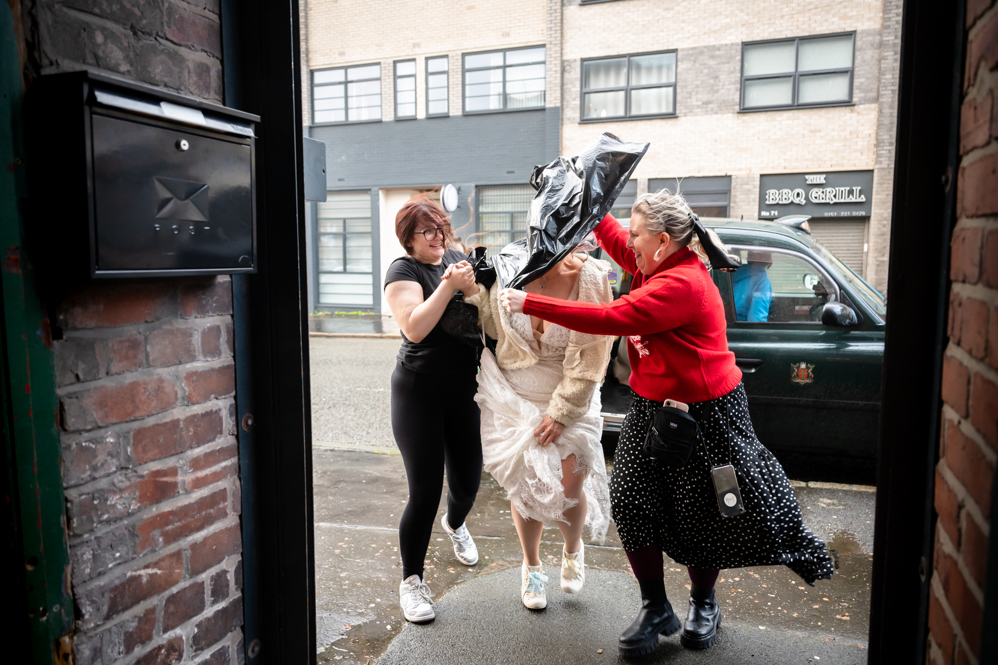 Bride arriving in the storm. She is covered with a bin bag to protect her hair.