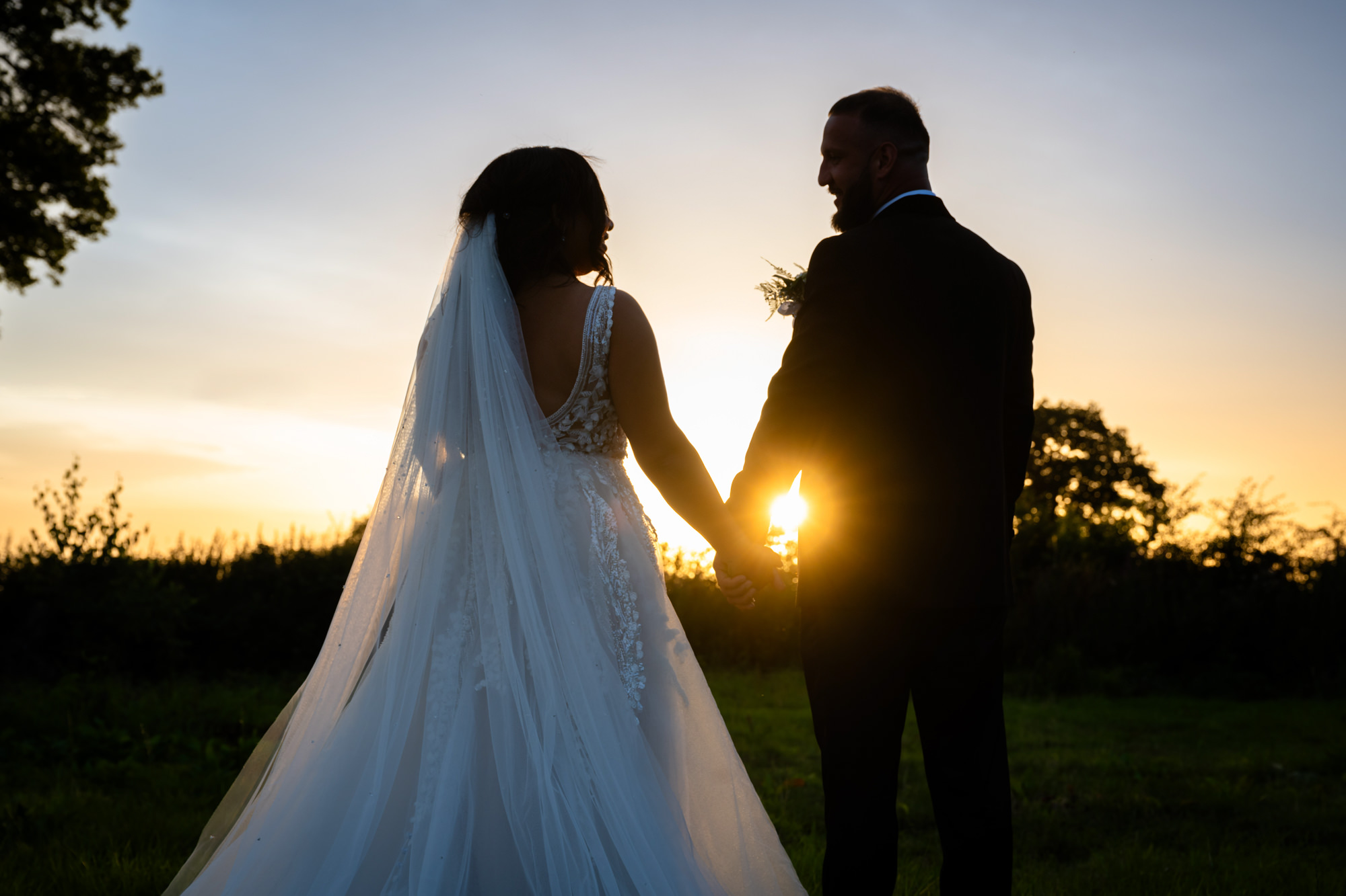 Bride and groom holding hands in the sunset at Hanbury Barns