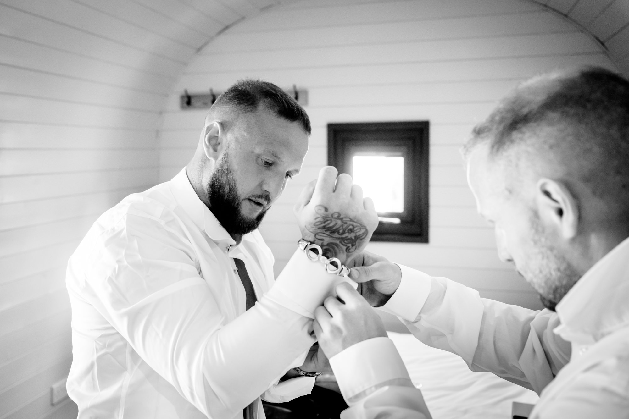 Best man helping the groom to put his cufflinks on in one of the pods at Hanbury Barns