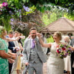 The happy couple exits the ceremony, walking down the aisle at Moddershall Oaks, with guests throwing confetti on them.