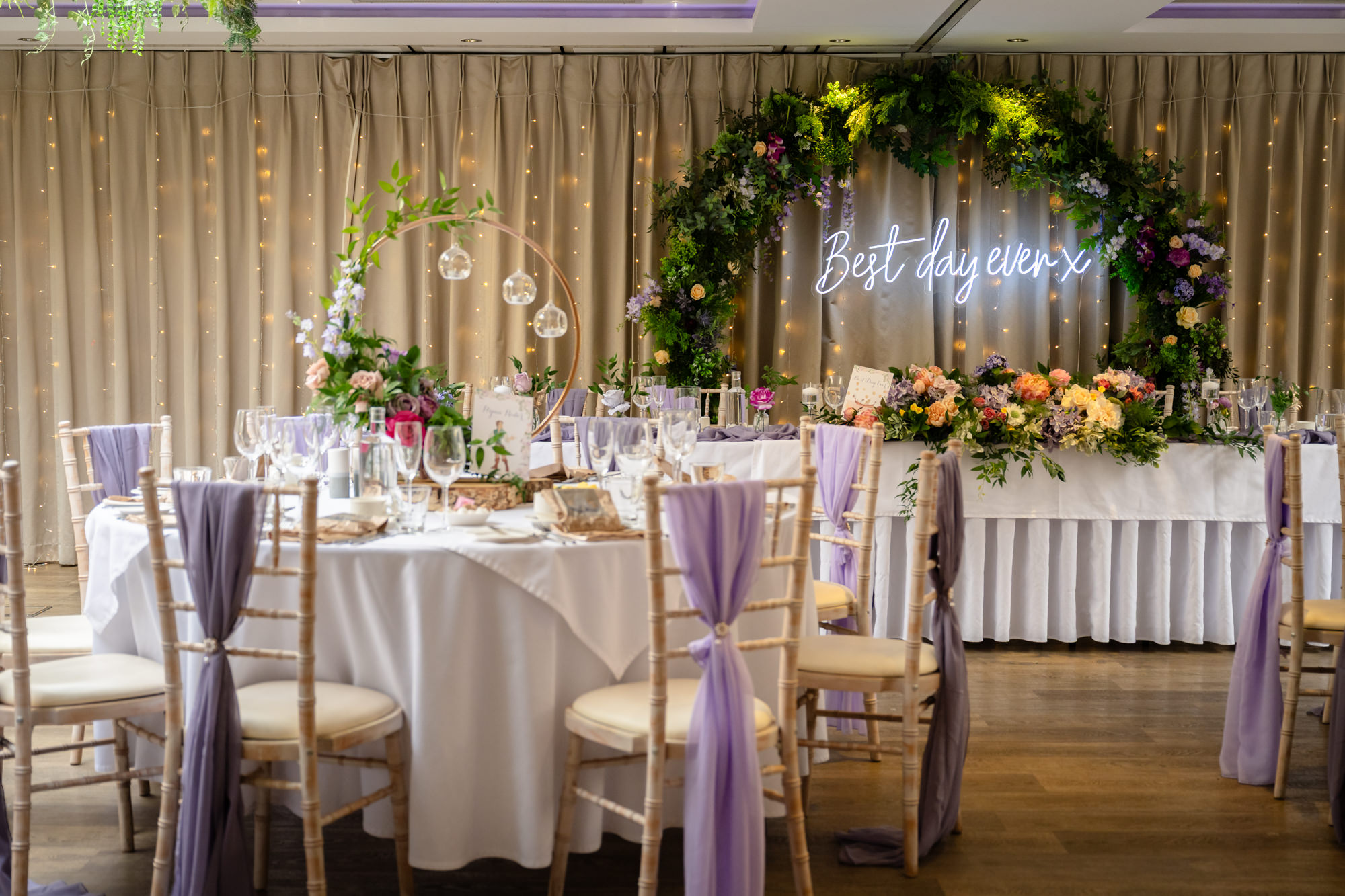 A beautifully decorated wedding reception room at Moddershall Oaks with white chairs, tables set with white tablecloths, and green floral accents, showcasing Disney's Tangled-themed wedding details.