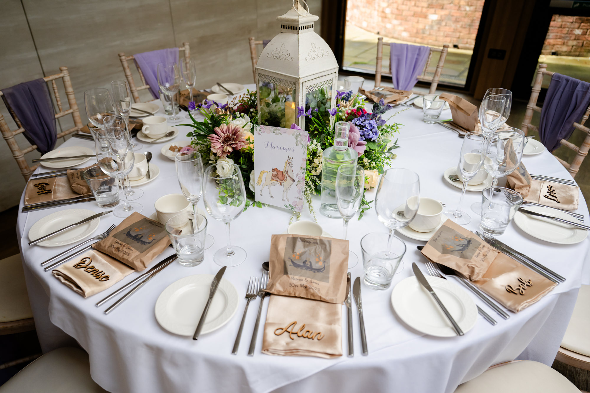 A perfectly set round wedding reception table at Moddershall Oaks with white tablecloths, green and purple floral centerpieces, and place settings for guests, reflecting Disney's Tangled-themed wedding details.