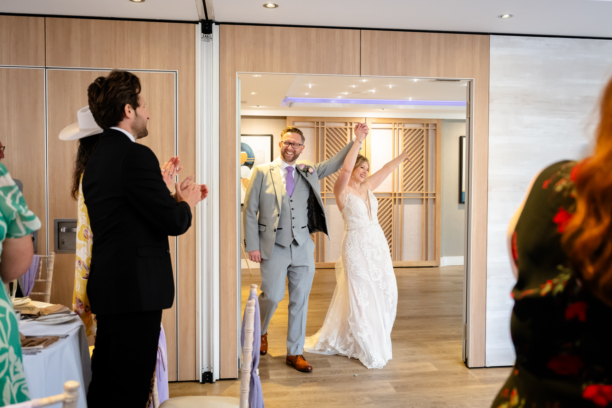 The bride and groom make a grand entrance into the reception room at Moddershall Oaks, with guests blurred in the foreground.