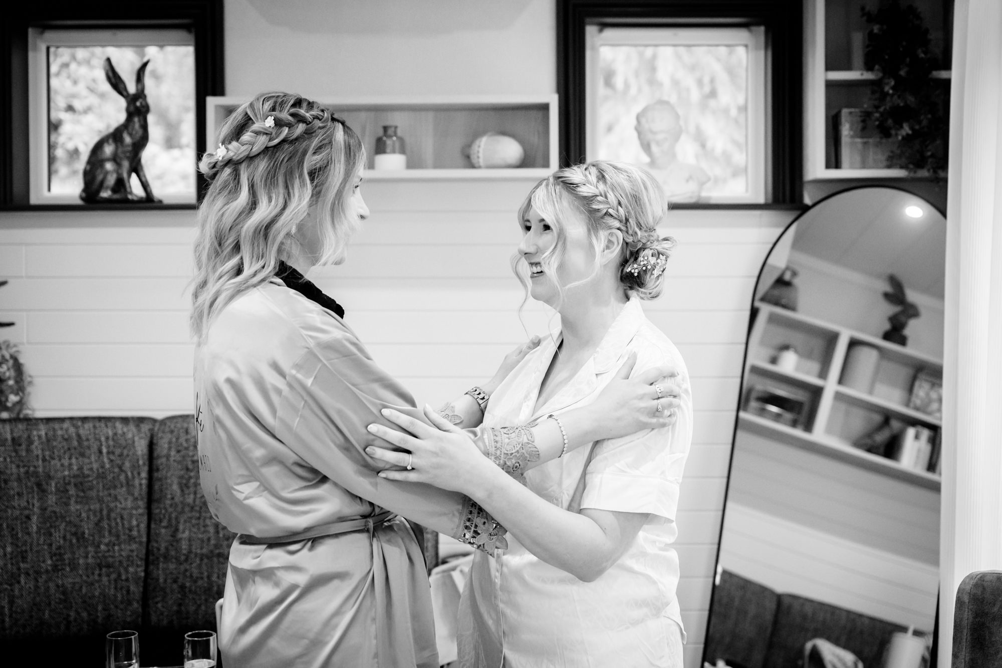 Two women in black and white, one with braided hair, embracing warmly and smiling, in the prep pod at Moddershall Oaks.