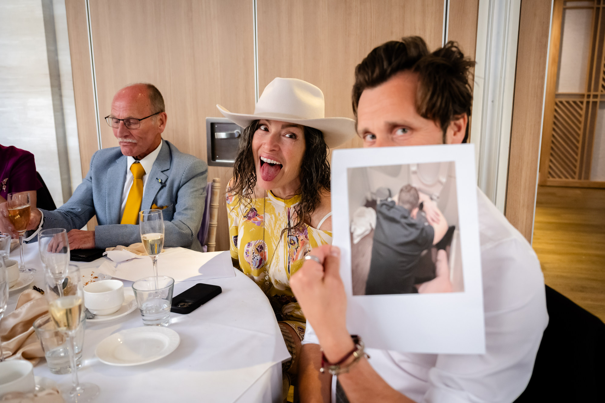 A guest holds up a small photo showing the groom in an embarrassing position, during the speeches at Moddershall Oaks.