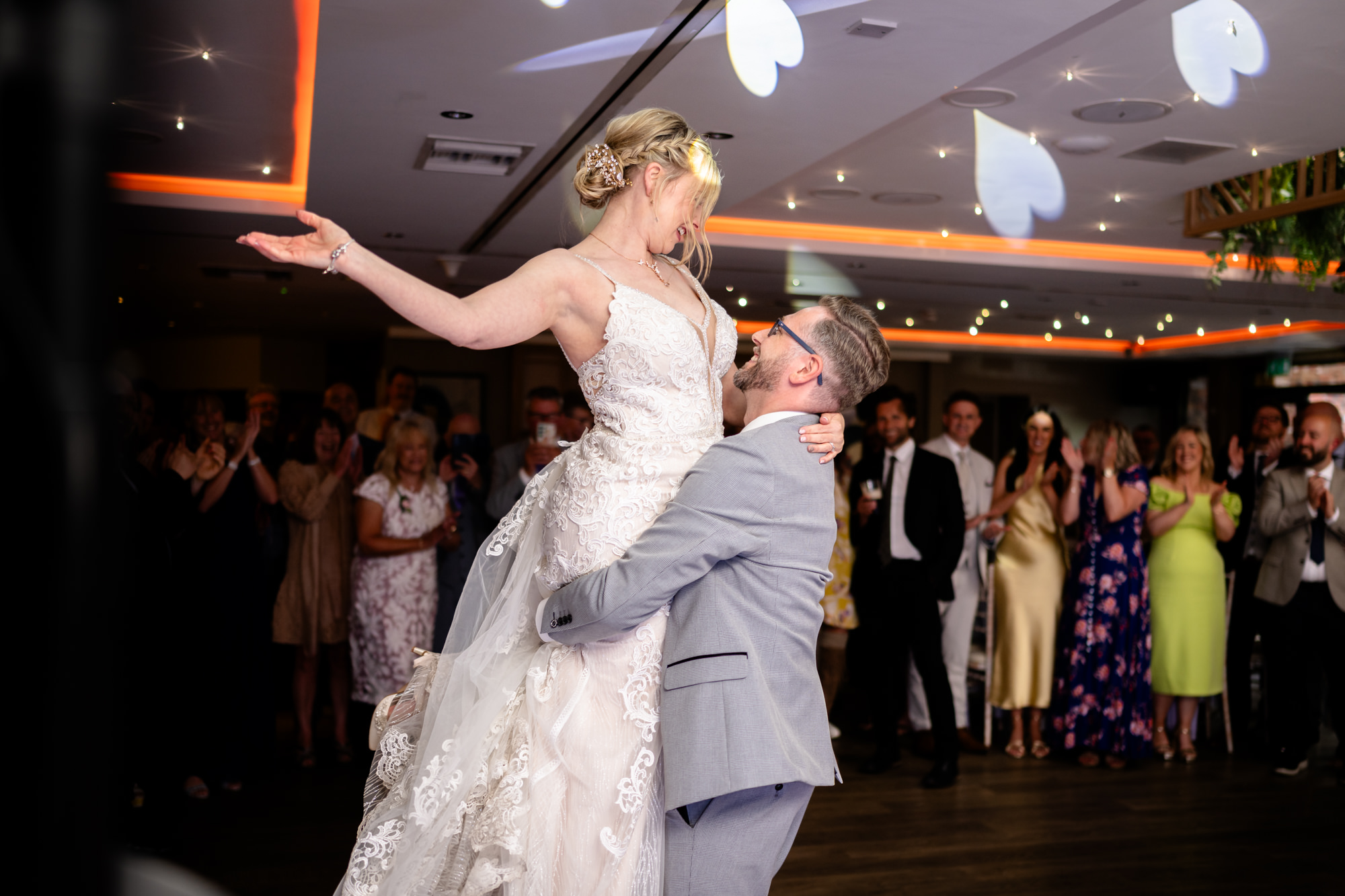 The bride is lifted up by the groom during a dance, with guests cheering around them on the dance floor, during their first dance at Moddershall Oaks.