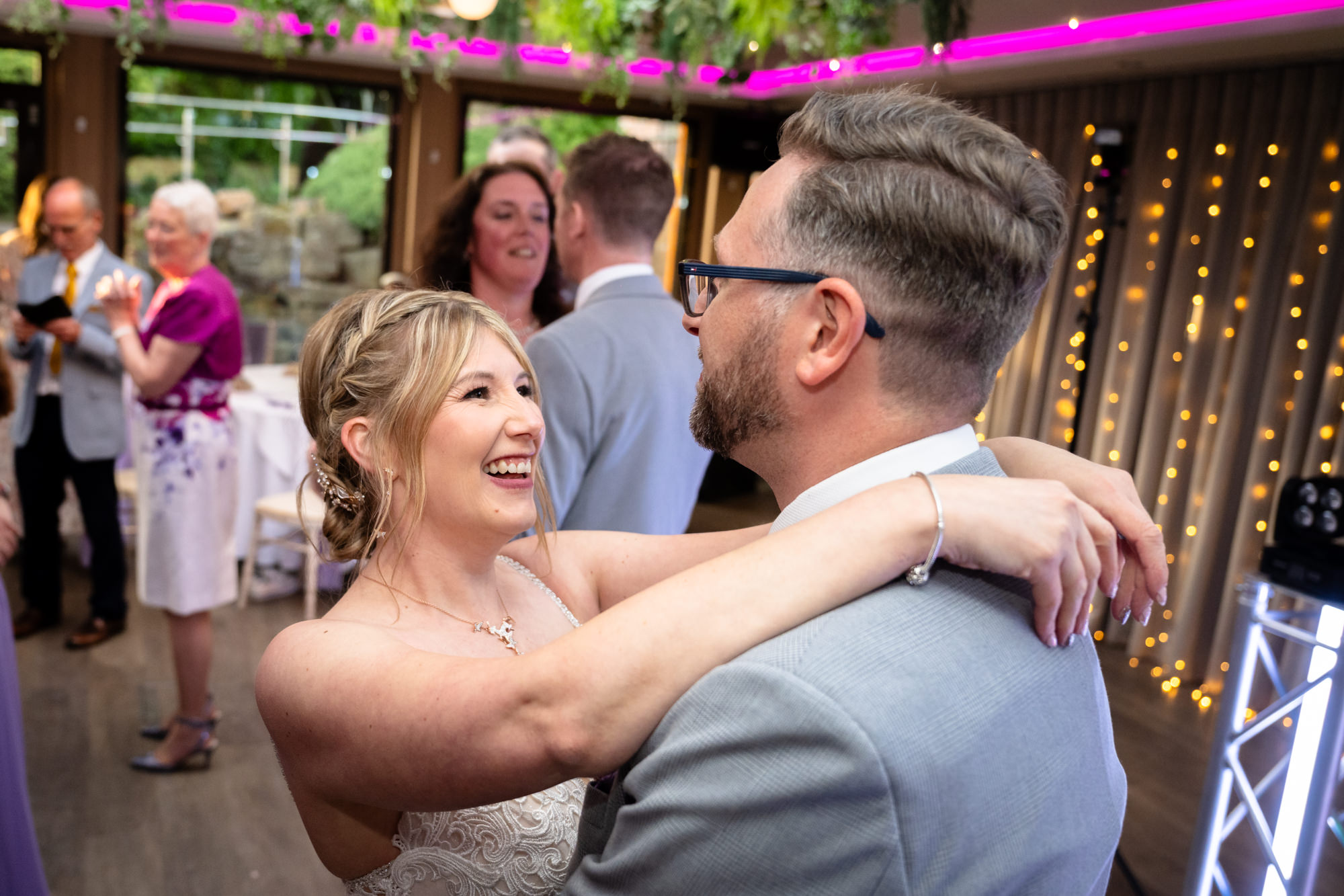 The bride and groom share a tender moment, embracing on the dance floor at Moddershall Oaks, bathed in party lights during the evening party.