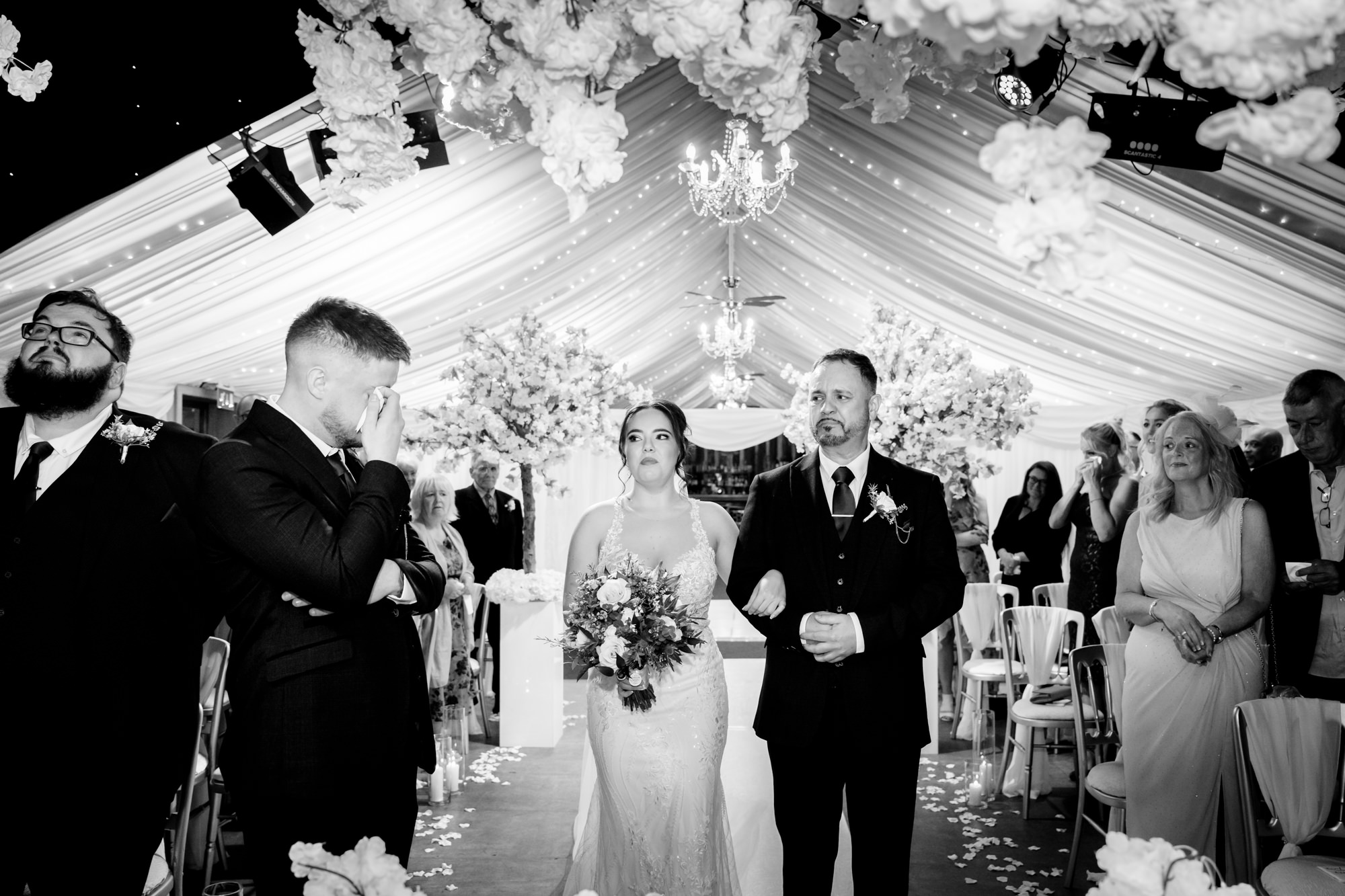 A wedding ceremony at Heaton House Farm where the bride walks down the aisle with her father, and guests are looking on.