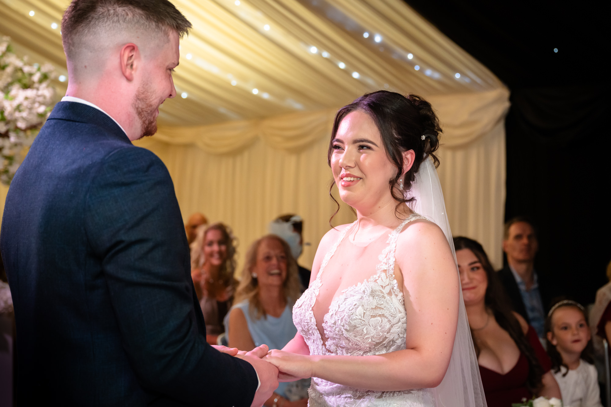 A moment from the wedding ceremony at Heaton House Farm as the bride smiles and looks at the groom.