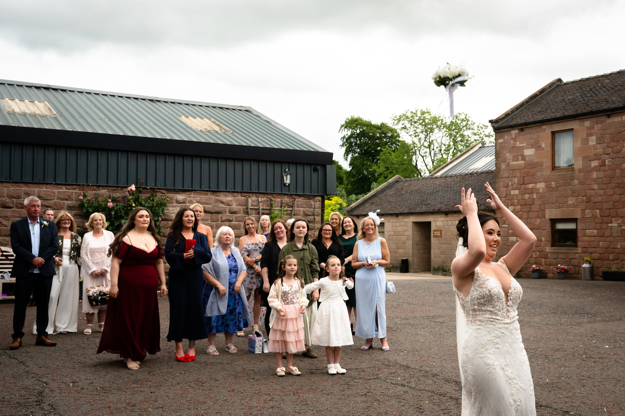 The bride, in her white dress, stands outside holding her bouquet as she prepares to throw it at Heaton House Farm.