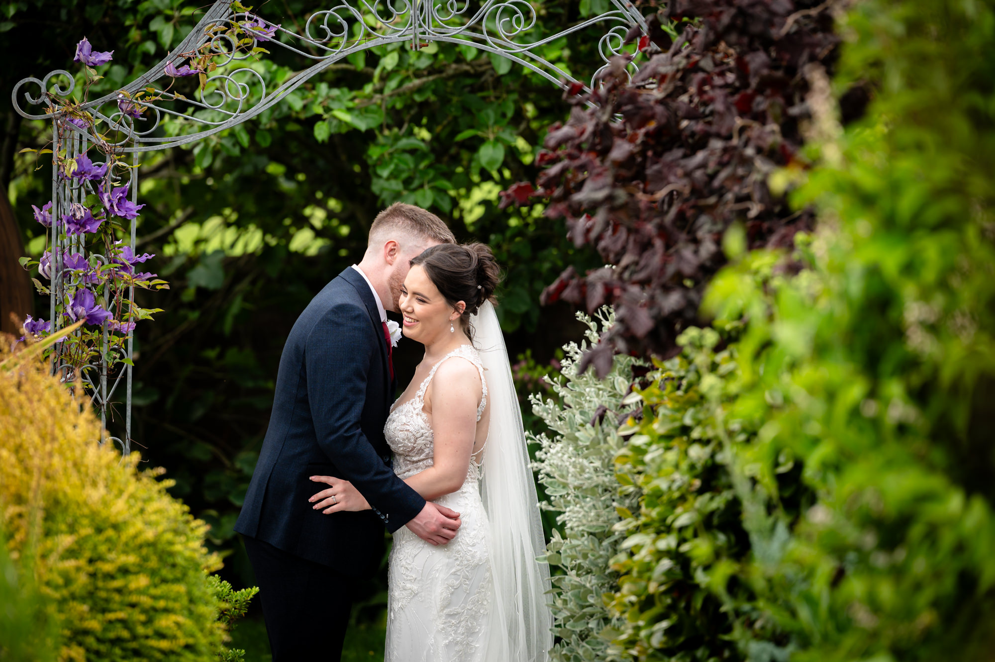 The bride and groom pose for a portrait photo outside at Heaton House Farm, surrounded by lush green foliage.