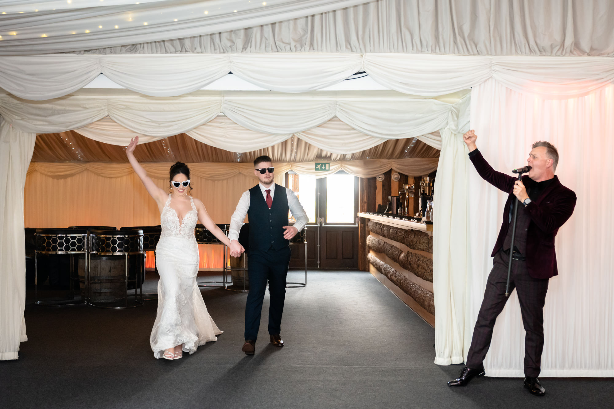 The bride and groom enter the wedding breakfast room at Heaton House Farm, with a singer performing in the foreground.