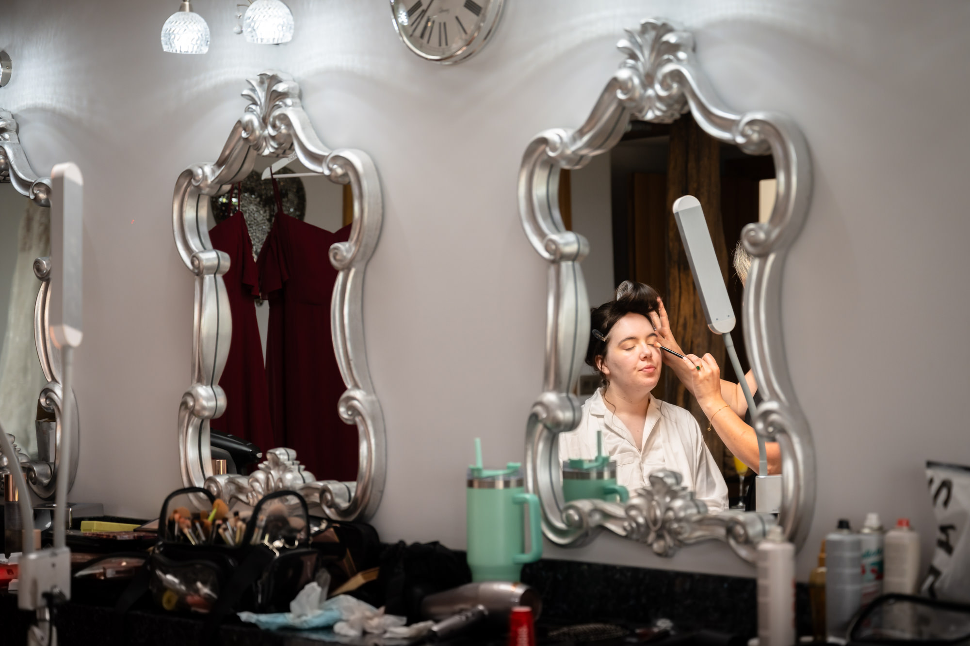 A full-color photo of the bride in a chair getting her makeup done in the Pamper room at Heaton House Farm.