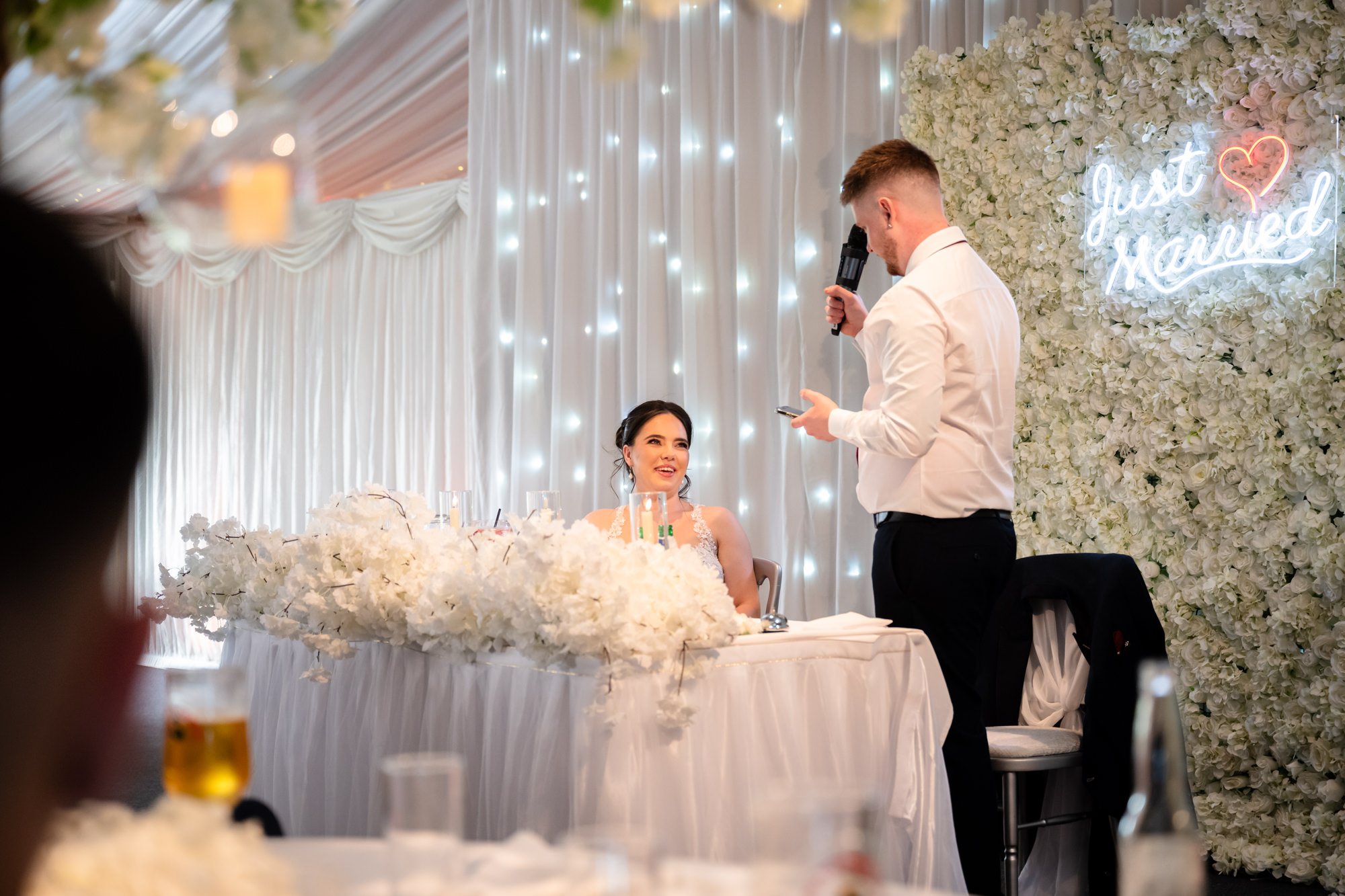 A candid shot of the bride smiling as the groom gives a speech at Heaton House Farm.