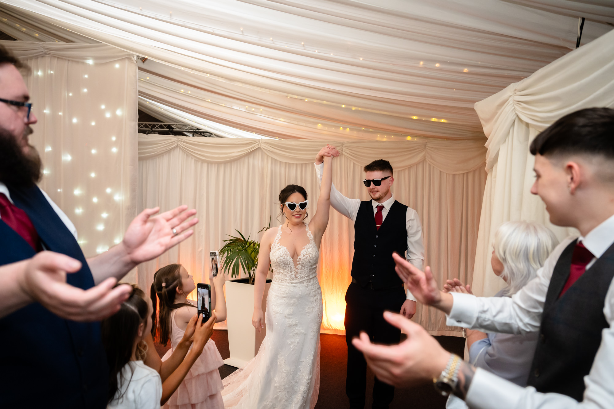 The bride and groom exit their reception, walking between two lines of guests clapping and celebrating their wedding at Heaton House Farm.