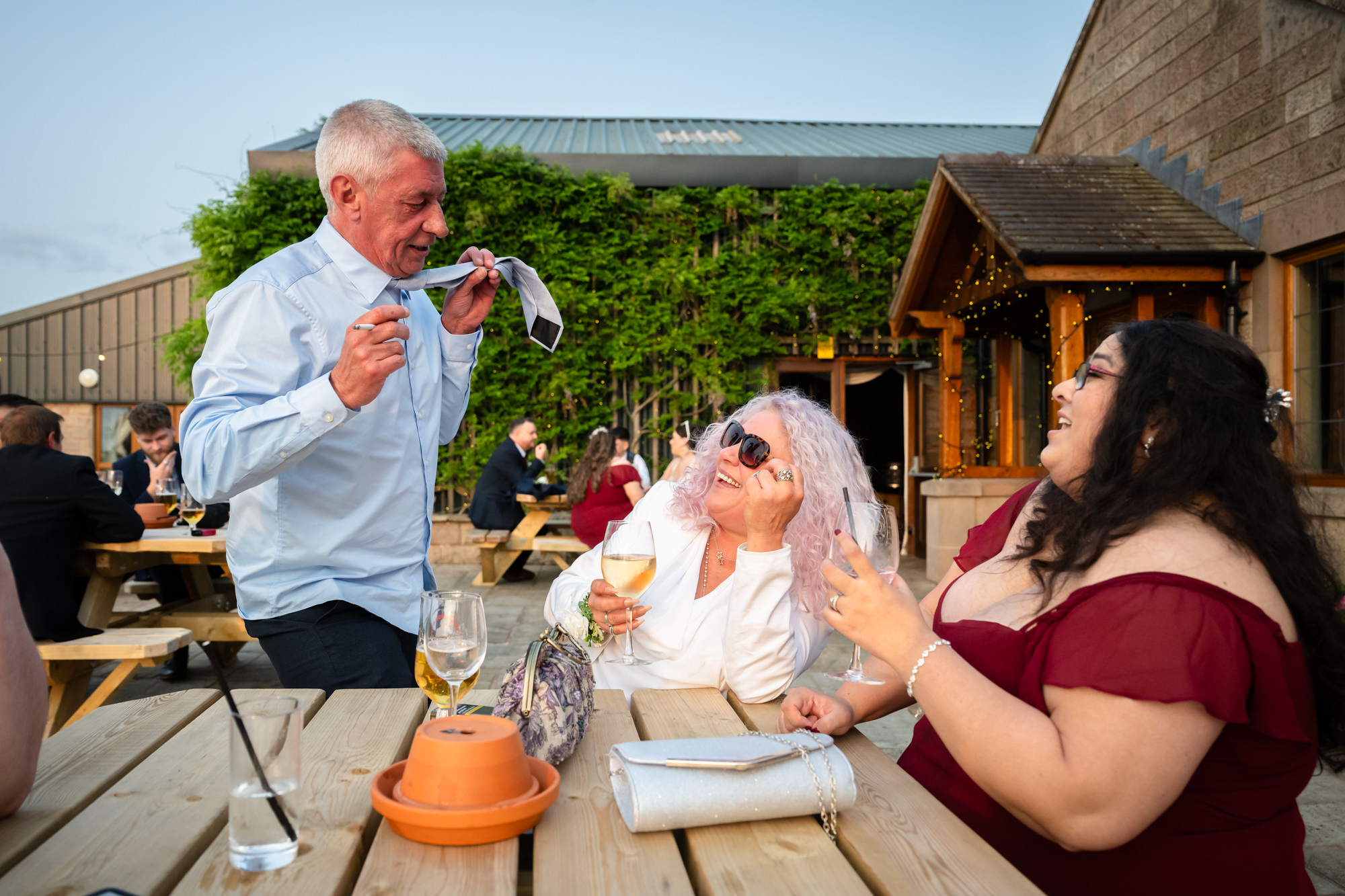 two wedding guests enjoy a drink with friends outside at Heaton House Farm.