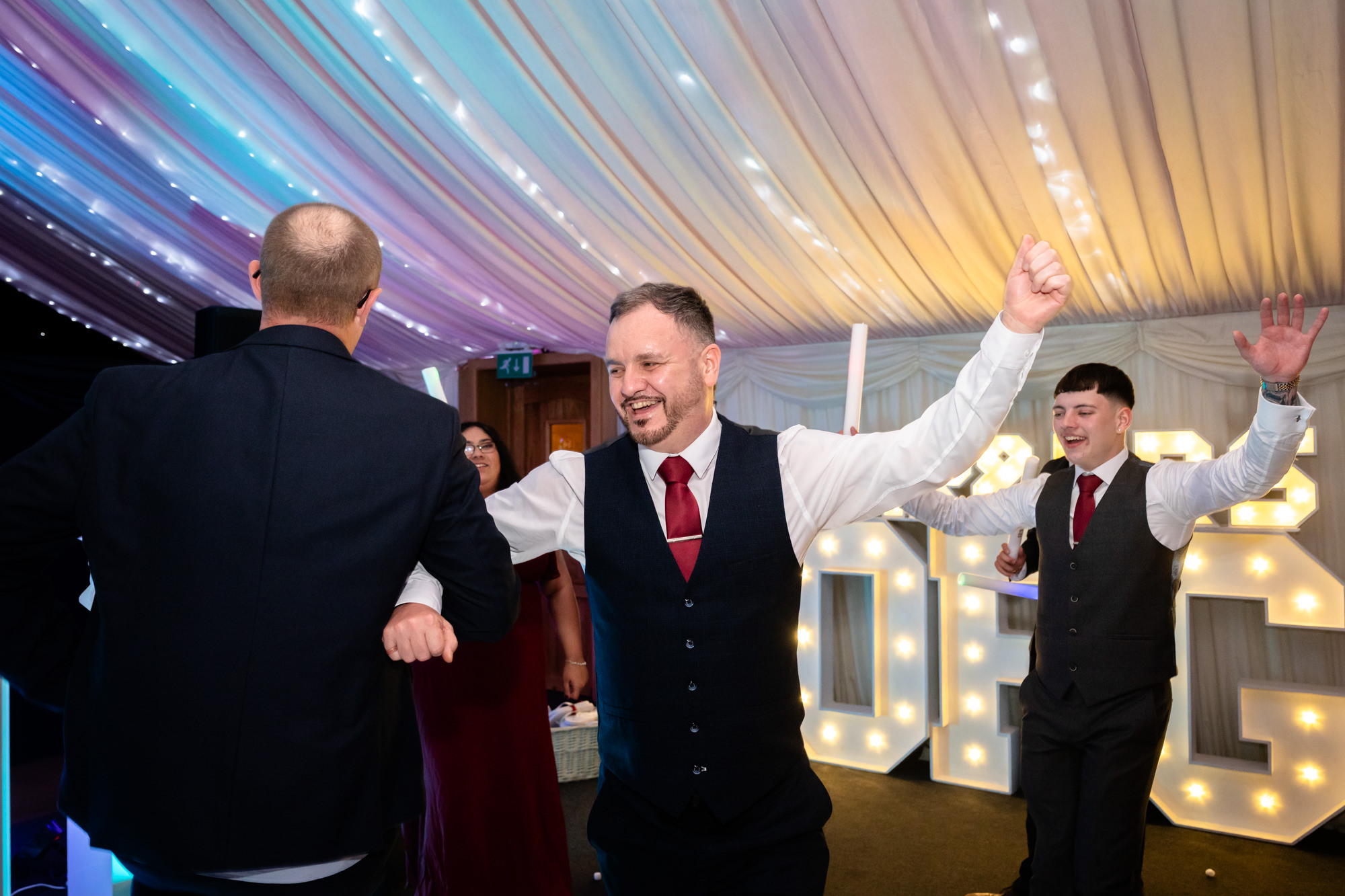 A man is dancing with a group of friends at the Heaton House Farm wedding party.