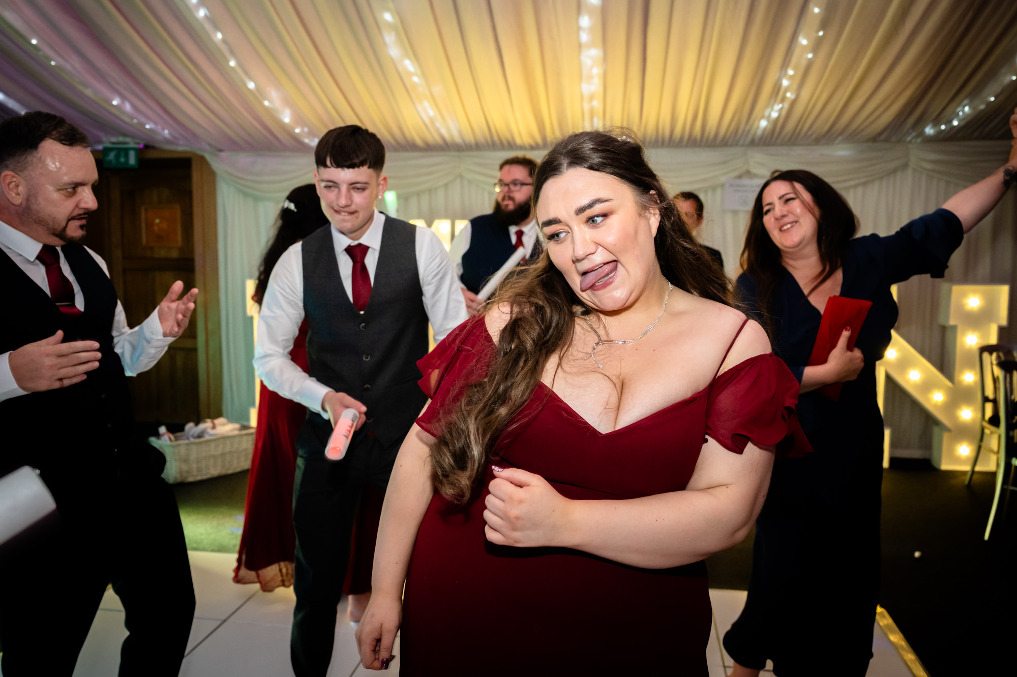 A woman with her arms crossed looks at the camera while her friends dance around her at the Heaton House Farm wedding party.