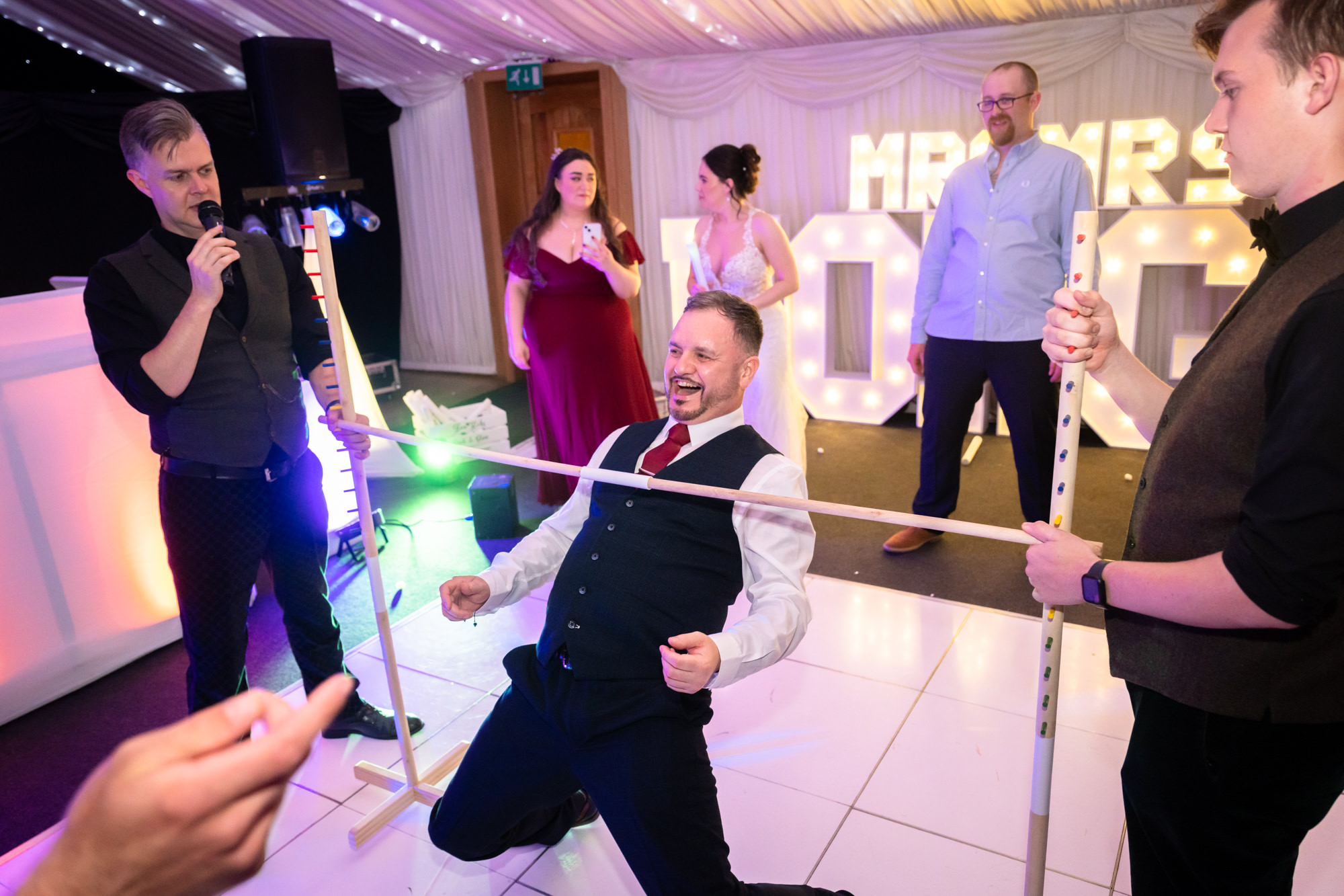 A man wearing a suit, vest, and tie is limbo dancing at the Heaton House Farm wedding party.