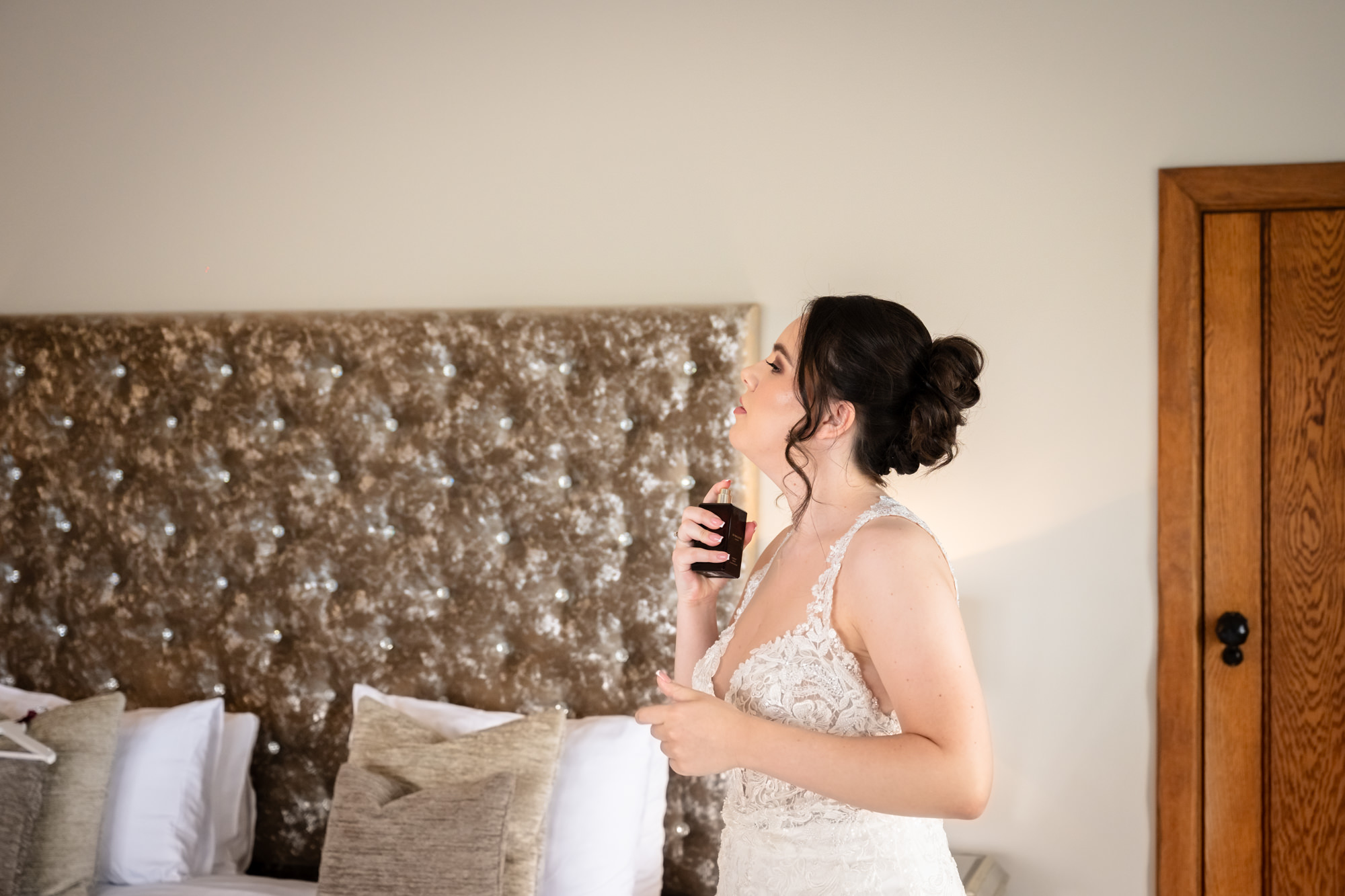 The bride, in her wedding dress, takes a final look at herself while spraying perfume at Heaton House Farm.