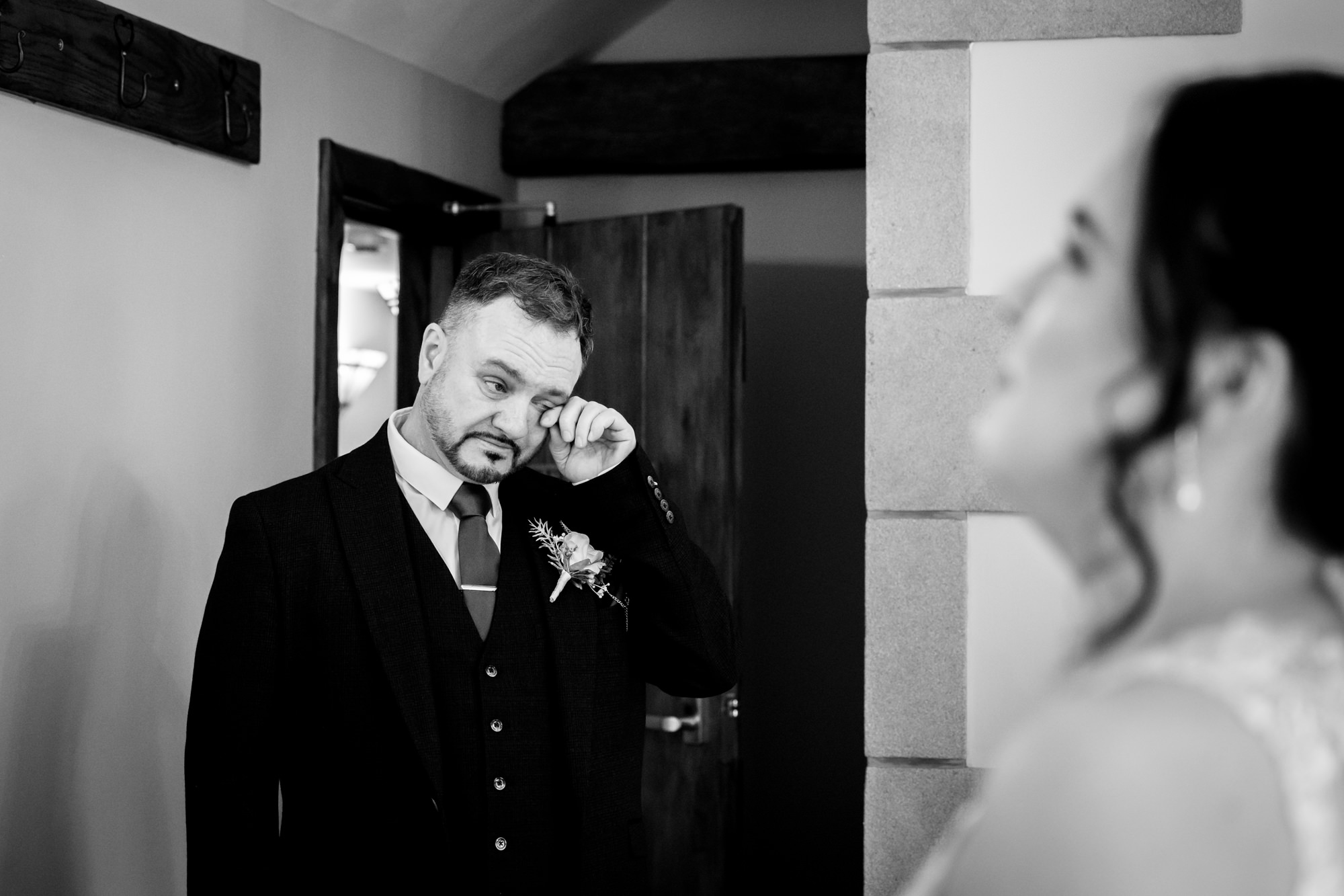 A black and white photo shows the emotional father of the bride wiping a tear from his eye as he looks at his daughter at Heaton House Farm.