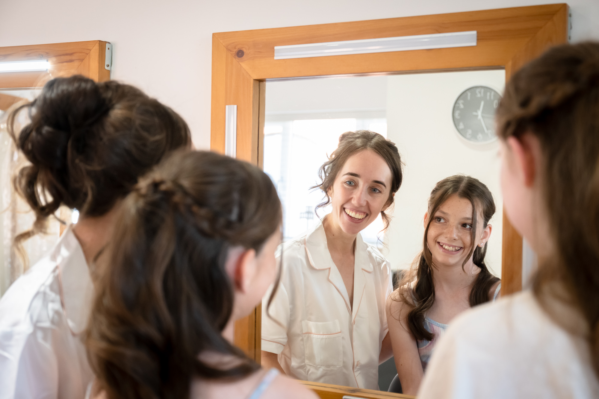 The bride and her flower girl smile at the reflection of themselves in a mirror, as they get ready for their wedding at Hanbury Barns.