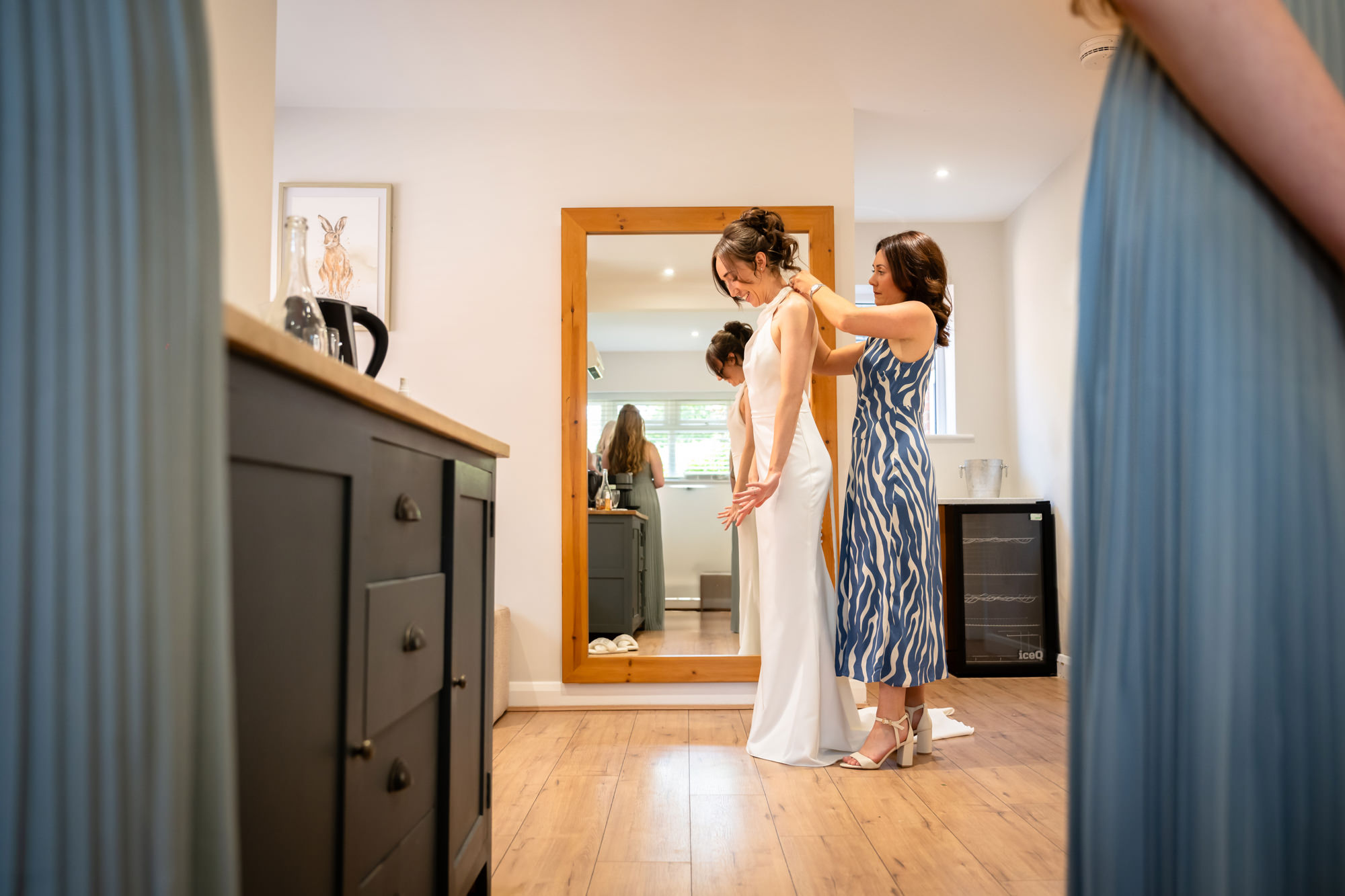 A woman helps the bride into her wedding dress in the dressing room at Hanbury Barns.