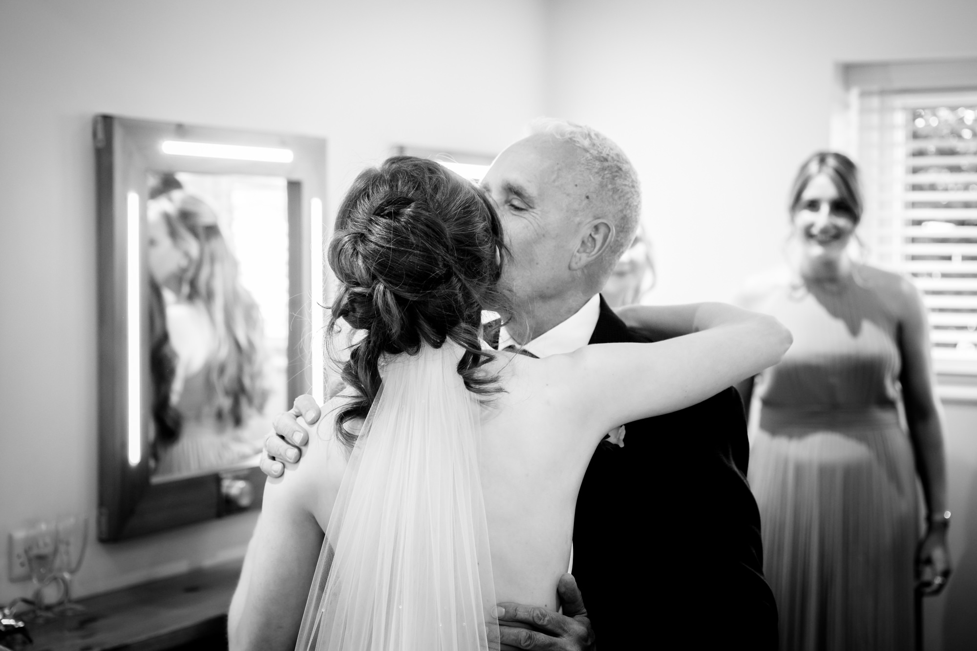 A black and white photo of an emotional father of the bride hugging his daughter at Hanbury Barns.