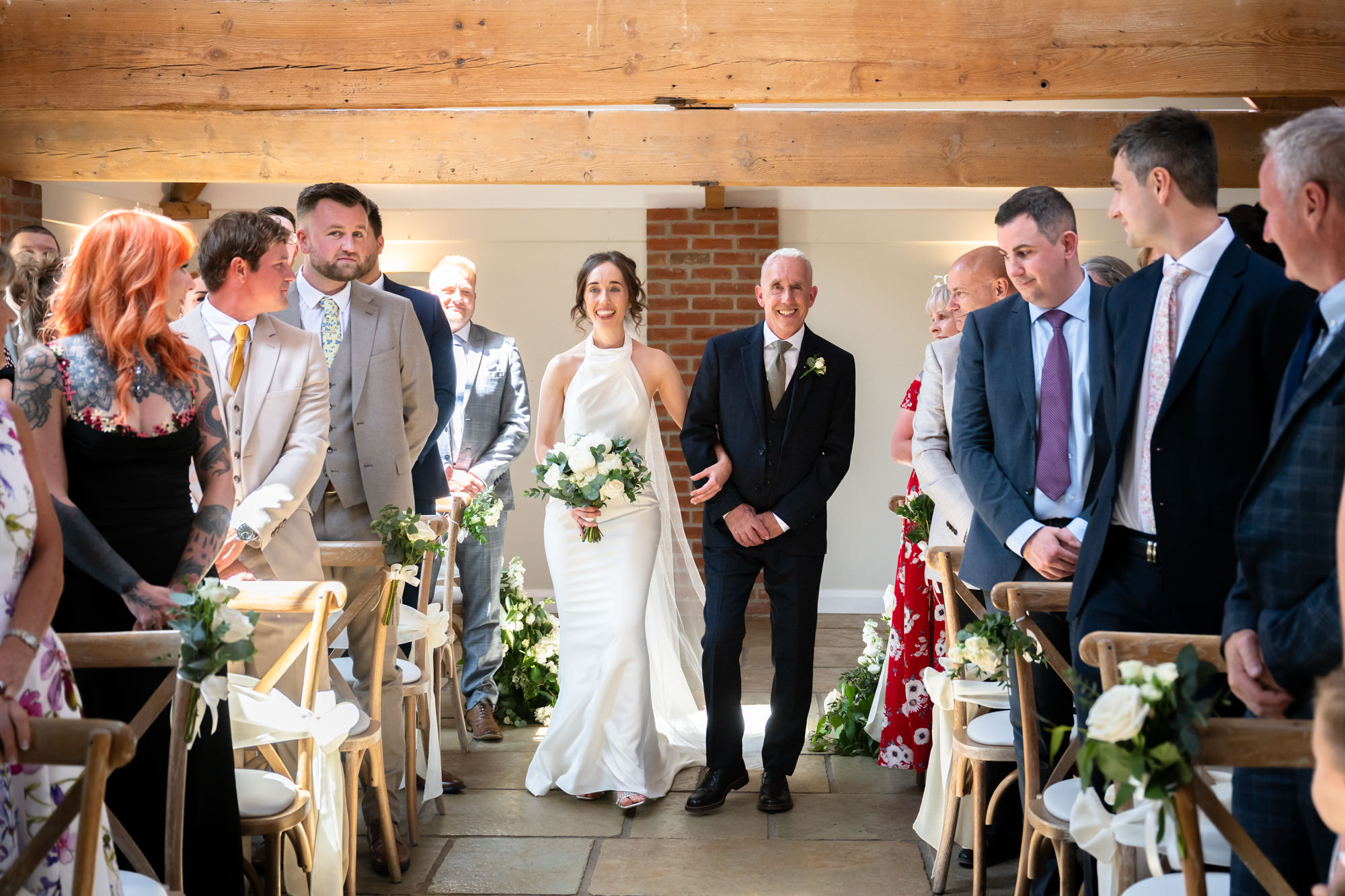 A wedding ceremony at Hanbury Barns with the bride being walked down the aisle by her father.