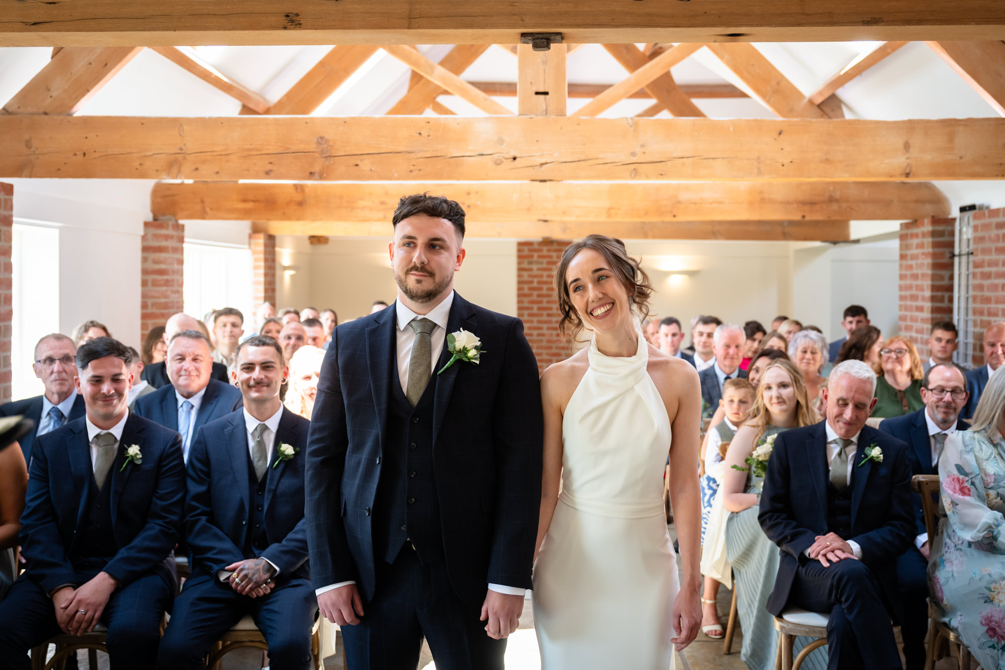 The bride and groom are standing together and looking out at the guests during their wedding ceremony at Hanbury Barns.