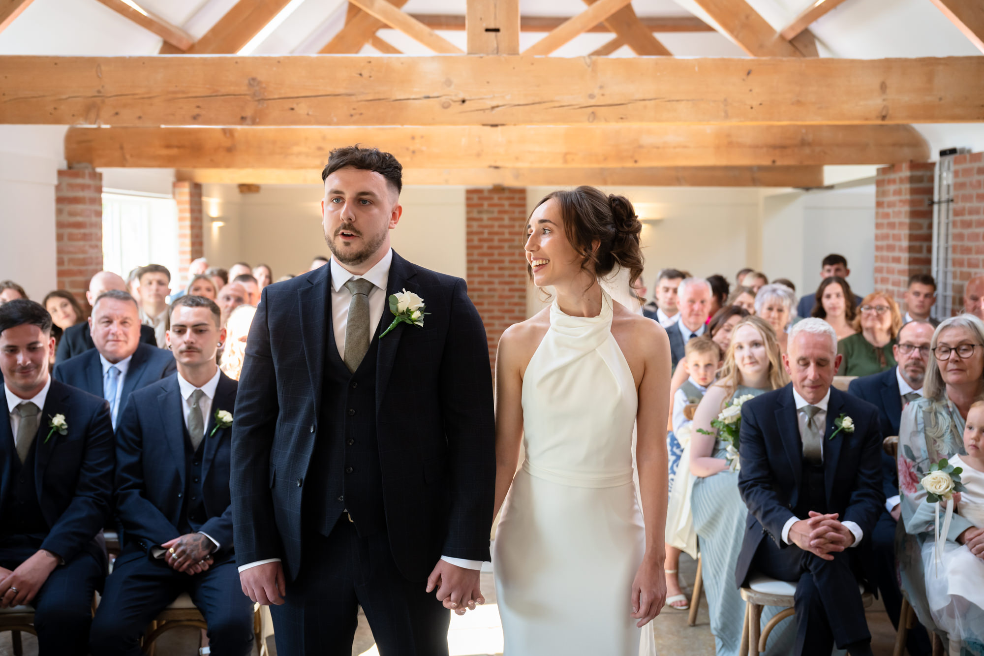 The bride and groom smile at each other during their wedding ceremony at Hanbury Barns.