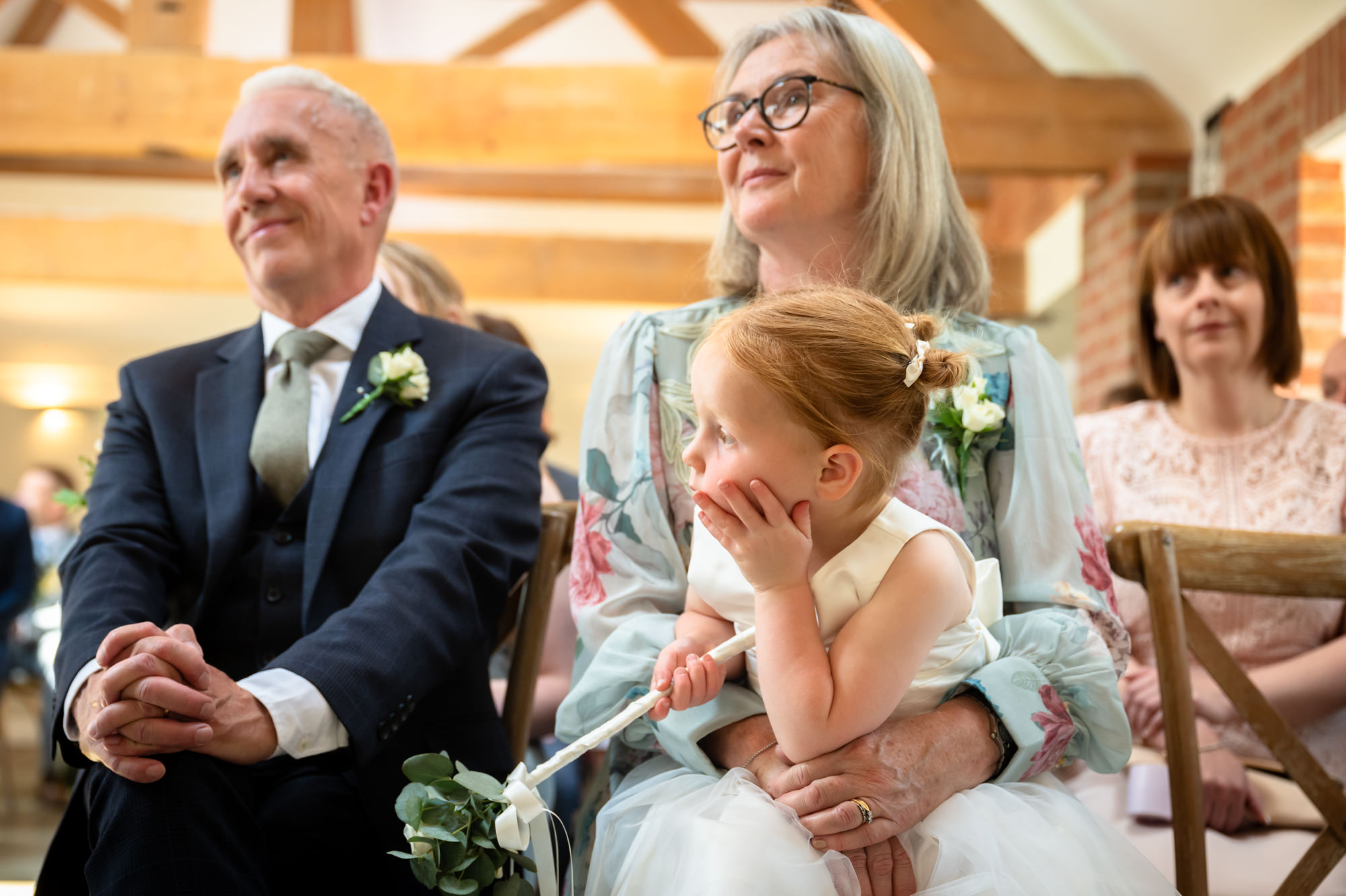 The flower girl sat on the front row with her hand on her chin.