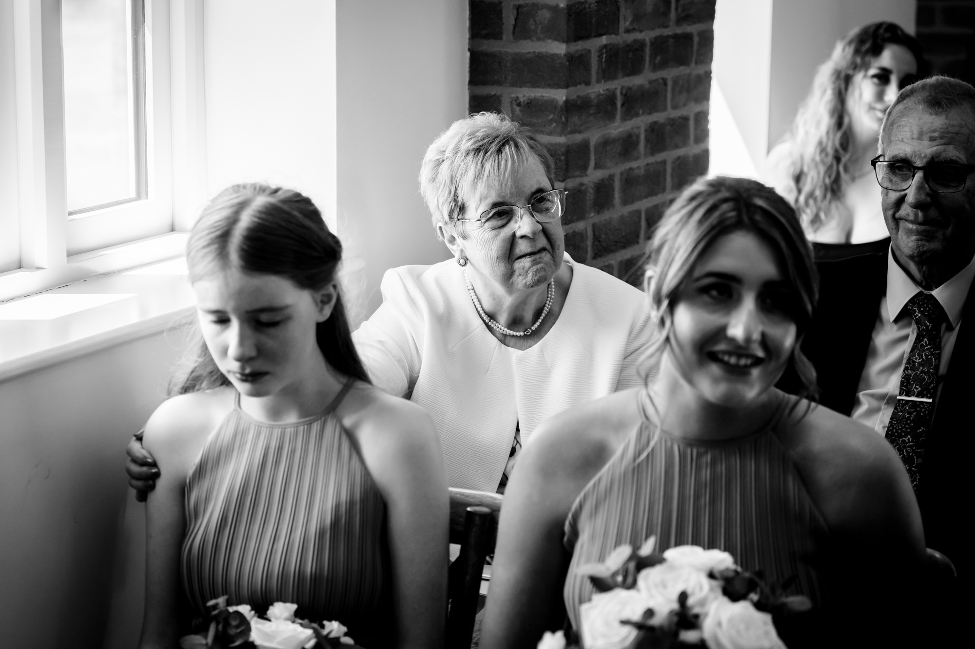 A black and white photo of two guests smiling during the wedding ceremony at Hanbury Barns.