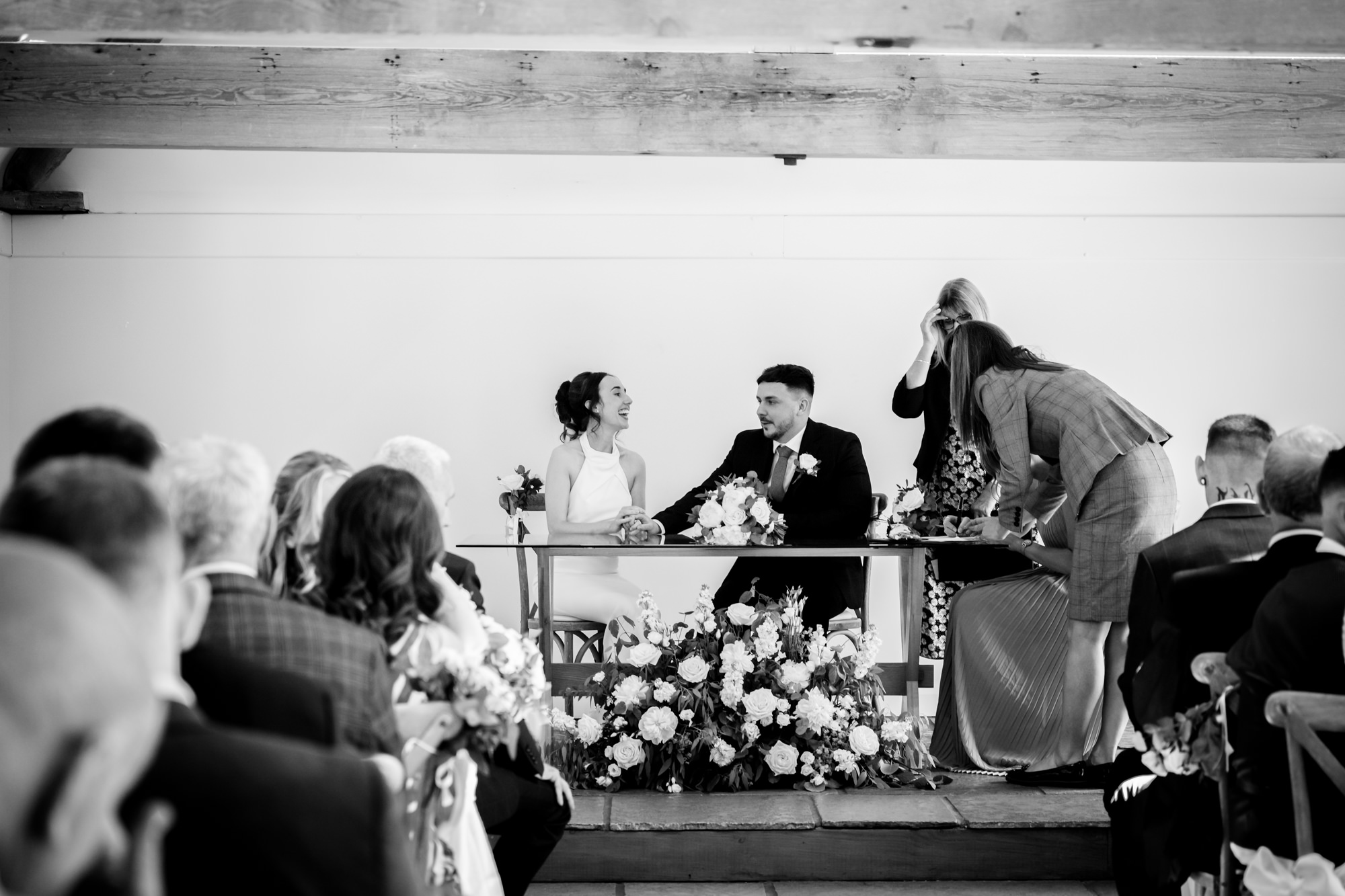 A black and white photo of the bride and groom signing the register at Hanbury Barns.
