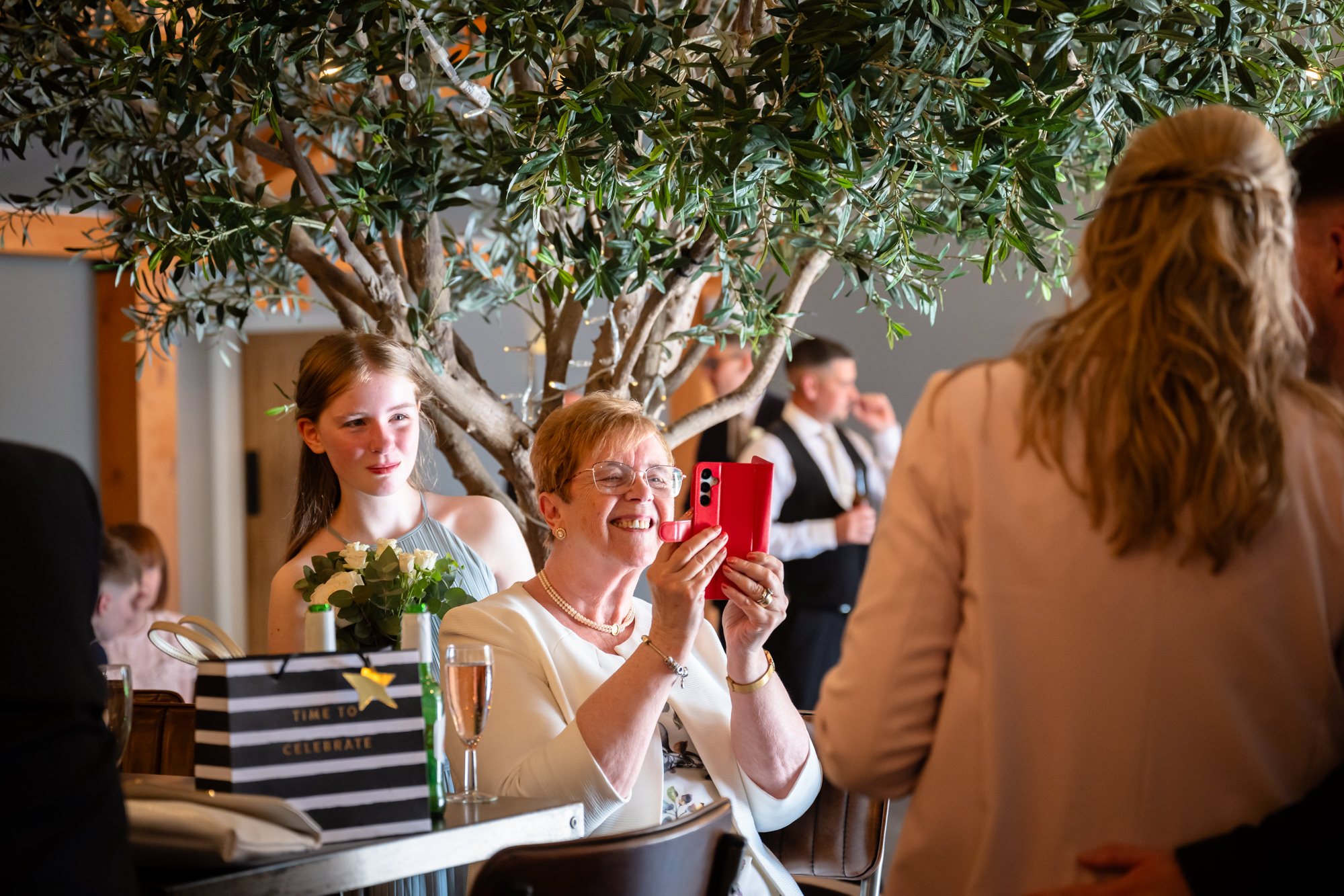 A guest is taking a photo on her phone while the bridesmaid is looking from behind
