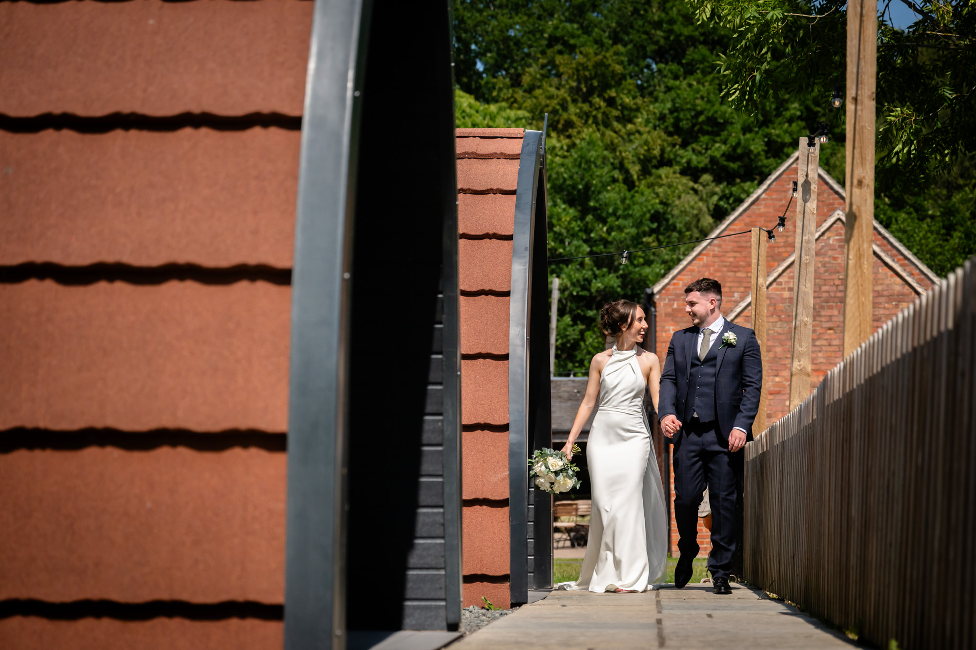 The bride and groom walk toward the camera from a distance, standing in a scenic outdoor area at Hanbury Barns.