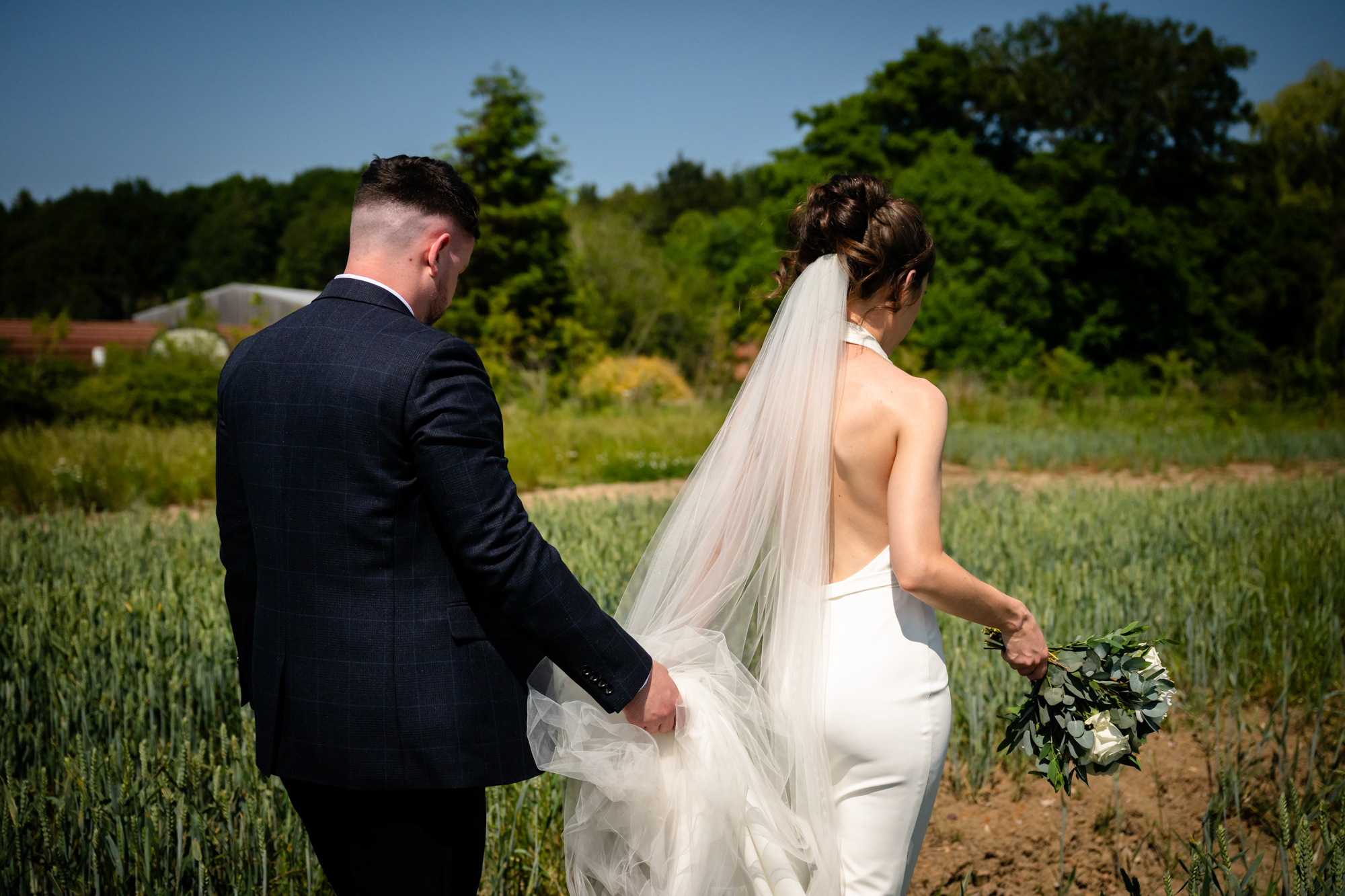 A portrait photo of the bride and groom captured from behind, as they walk away from the camera in a field at Hanbury Barns.