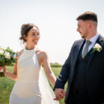 The bride and groom are captured in a portrait photo, holding hands and smiling at each other at Hanbury Barns.