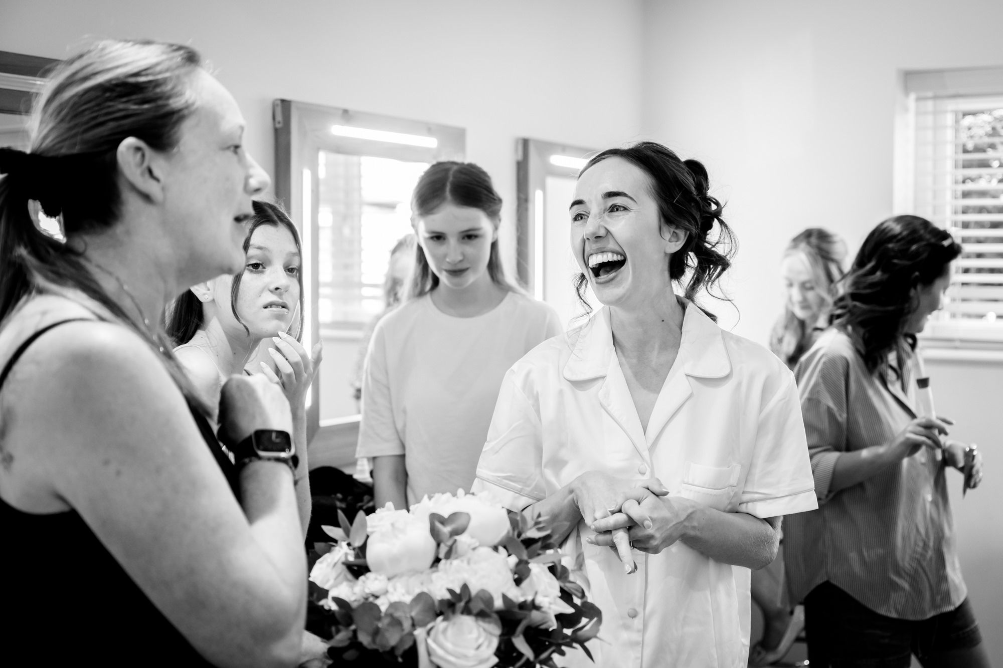 A candid, black and white shot of the bride laughing with her bridal party during bridal prep in the dressing room at Hanbury Barns.