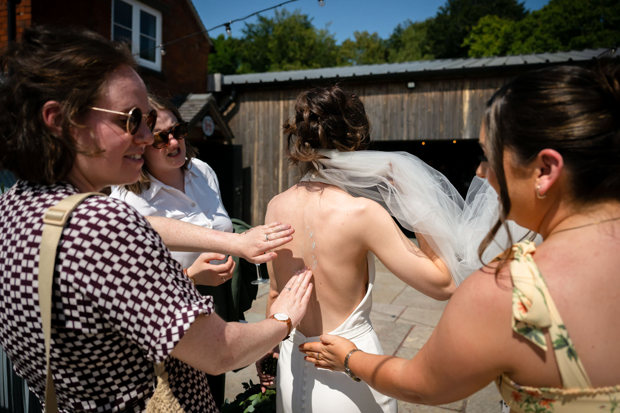 Guests applies sun cream on the bride's back at the wedding at Hanbury Barns.