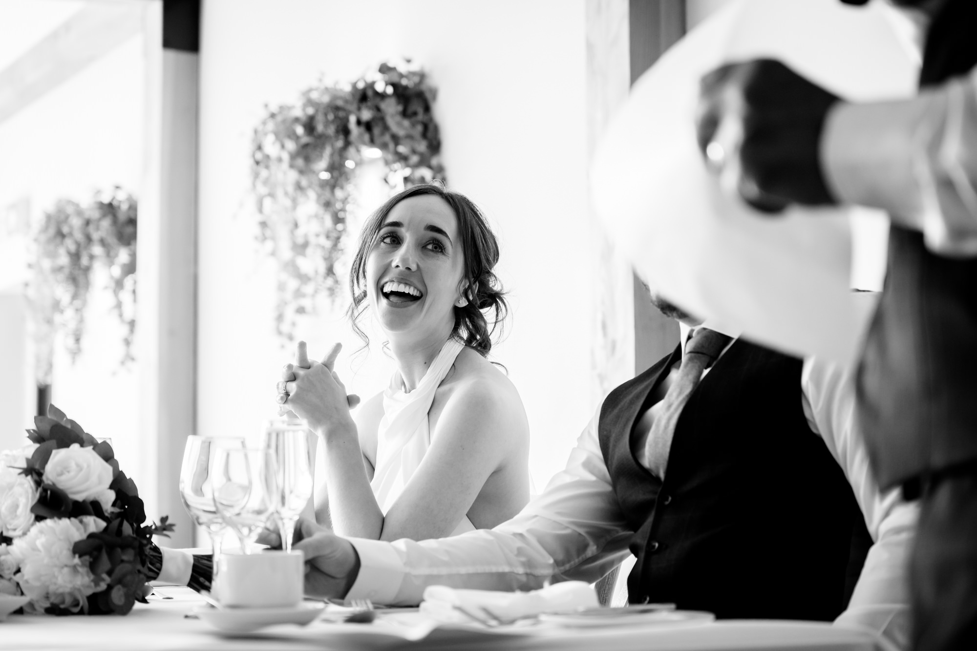 A black and white shot of the bride laughing while sitting at a table at Hanbury Barns.