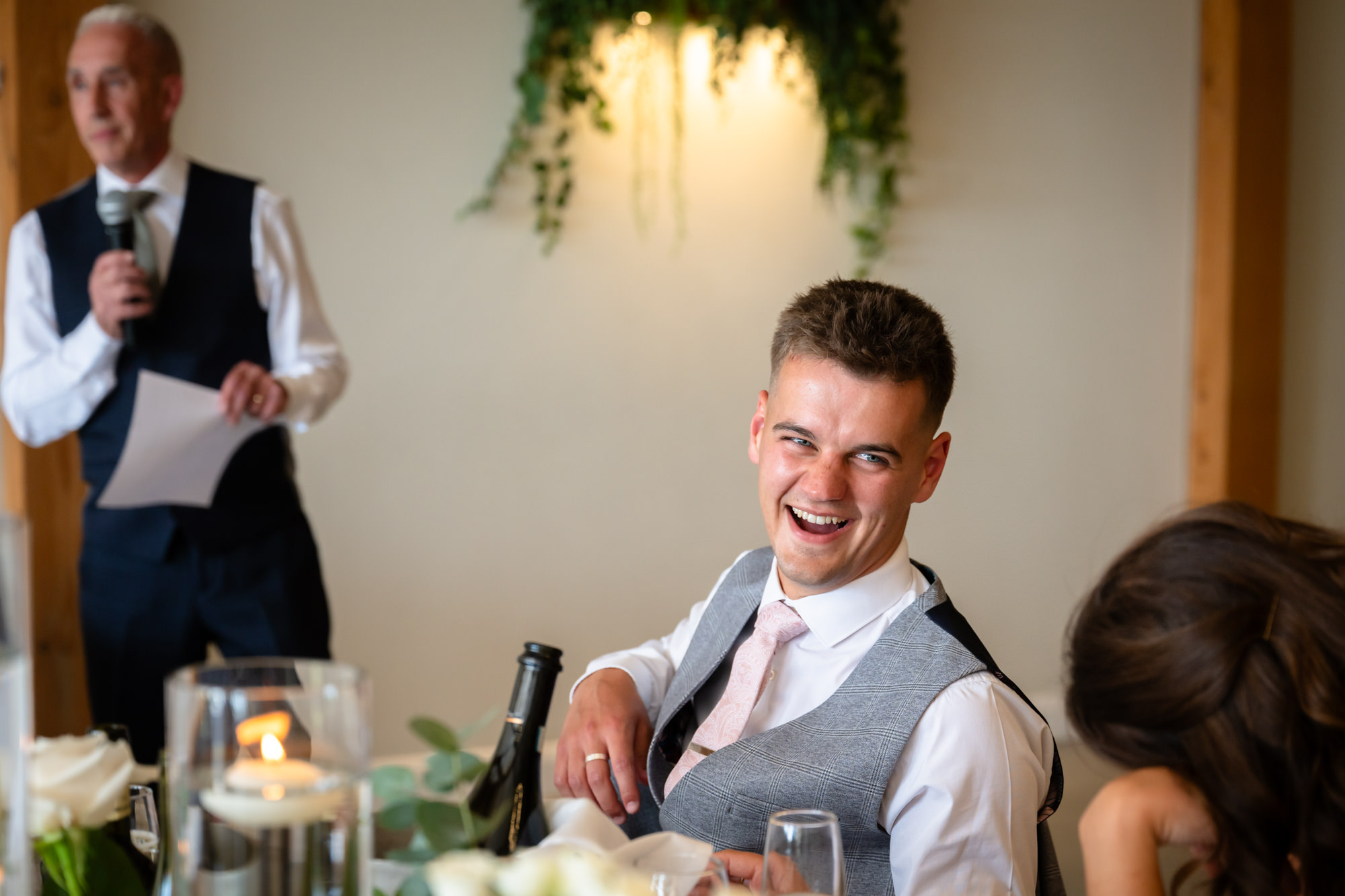 A candid shot of a guest laughing while another man gives a speech at Hanbury Barns.