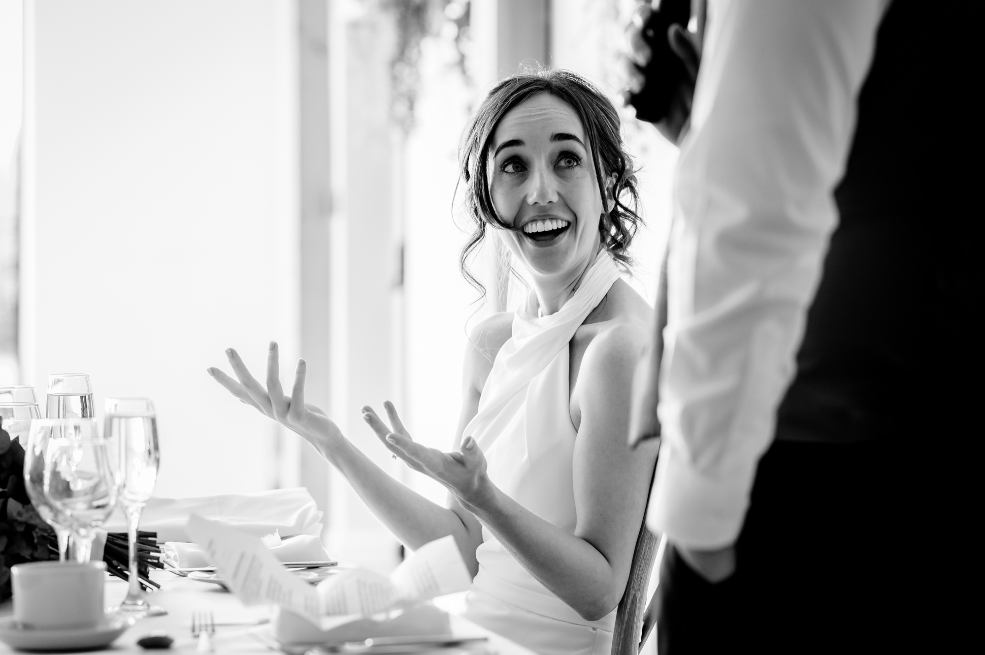 A black and white photo of the bride in a white outfit, laughing with her arms up in the air at the reception at Hanbury Barns.