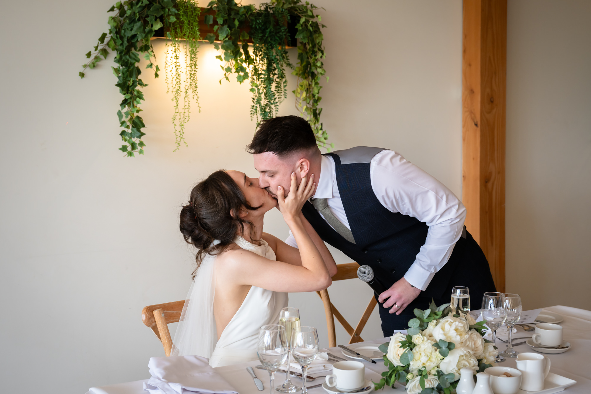 A candid shot of the bride and groom kissing while seated at a table at Hanbury Barns.